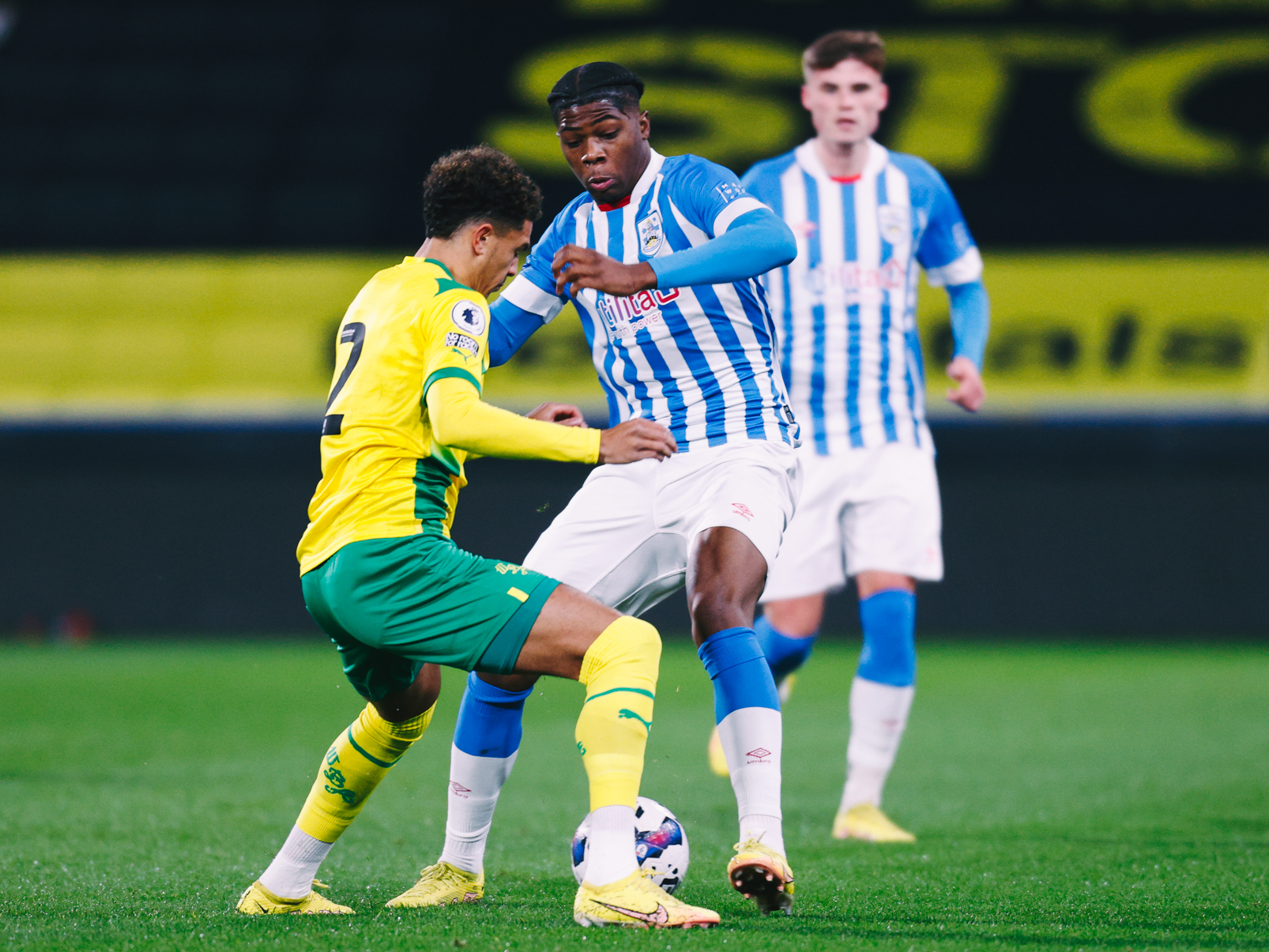 Ethan Ingram challenges a Huddersfield Town defender for the ball in the Premier League Cup