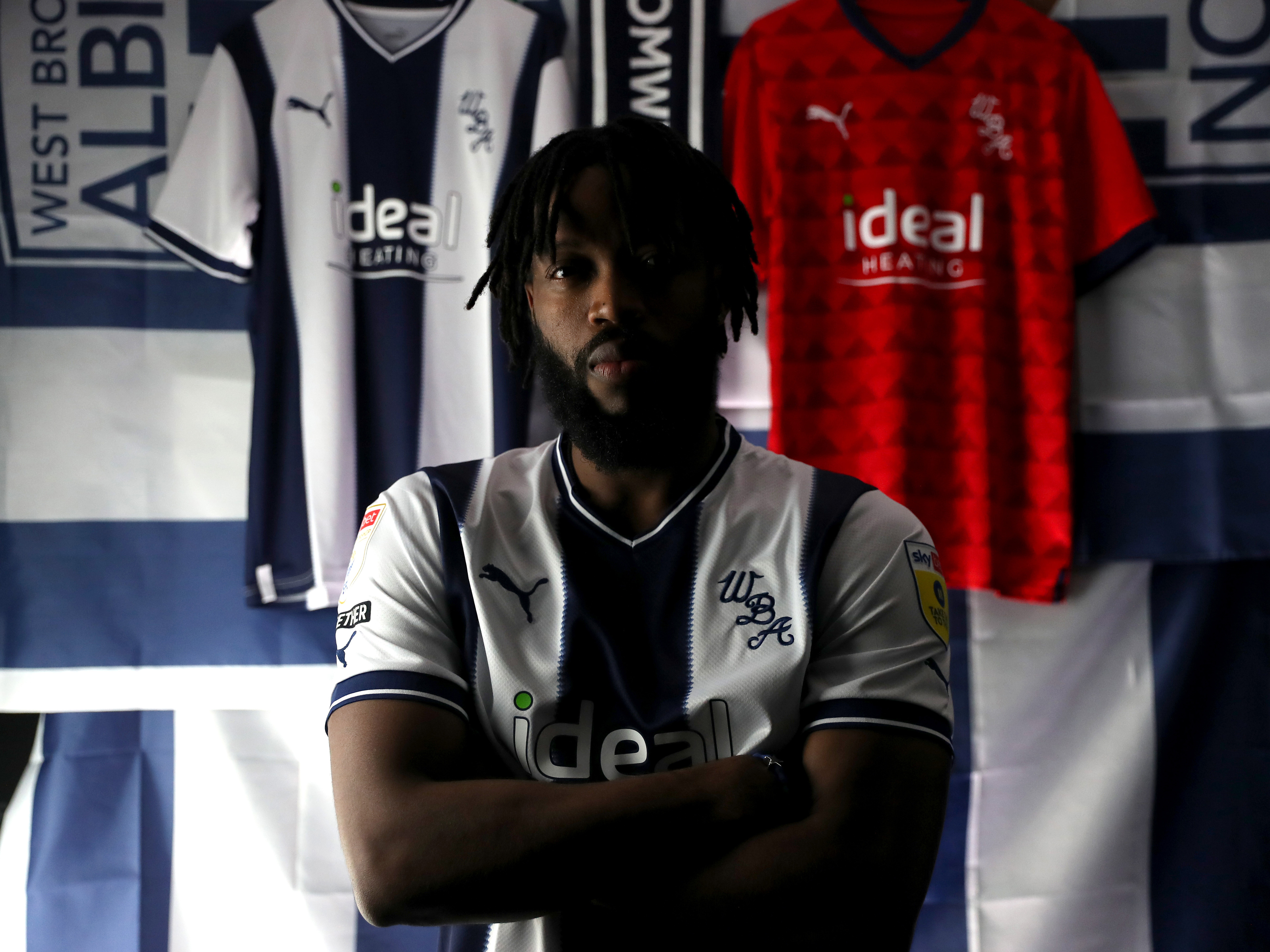 Nathaniel Chalobah poses in the home kit in front of two more Albion shirts