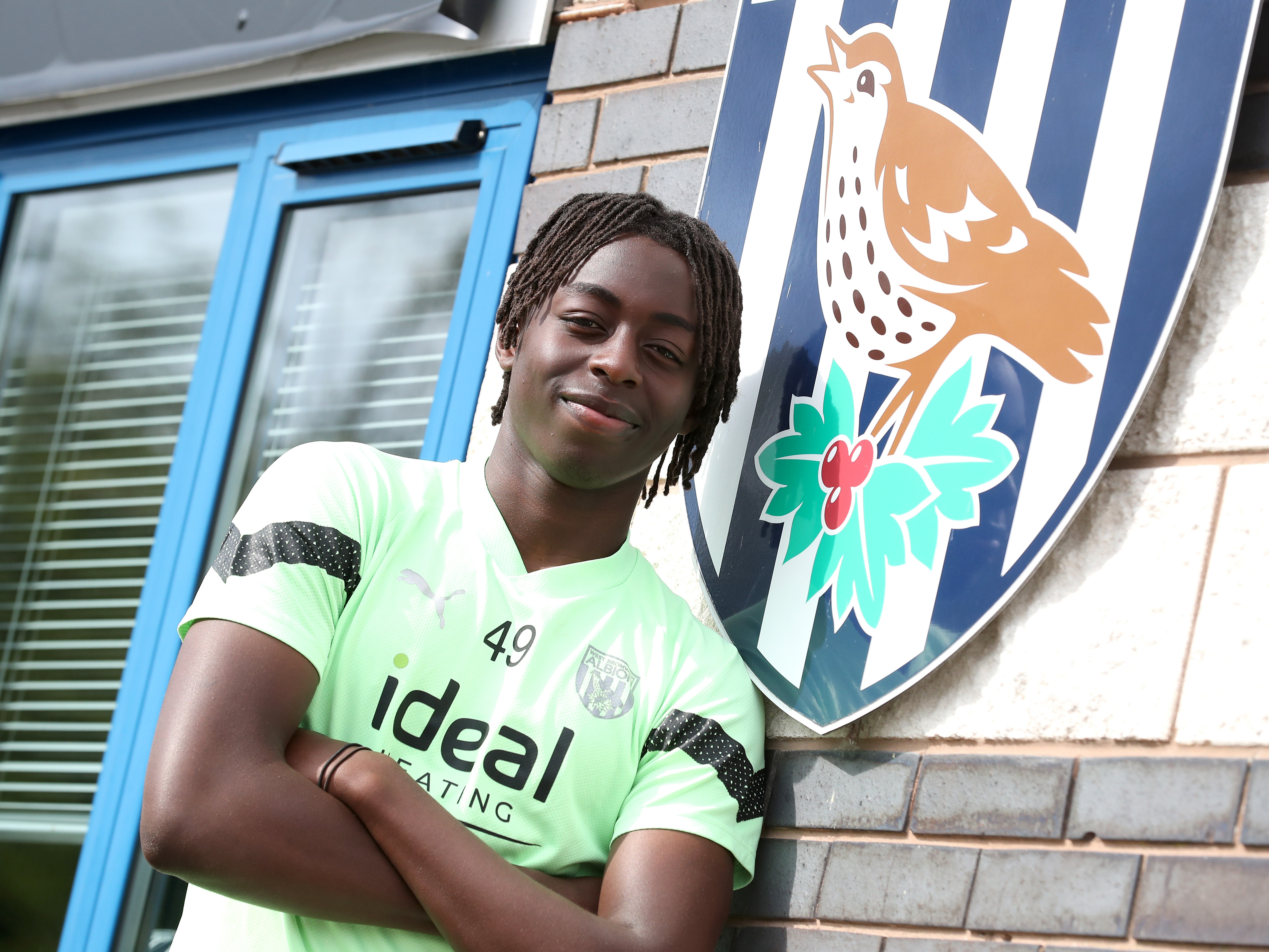 A photo of Albion youngster Eseosa Sule in front of the club crest outside the trainIng ground