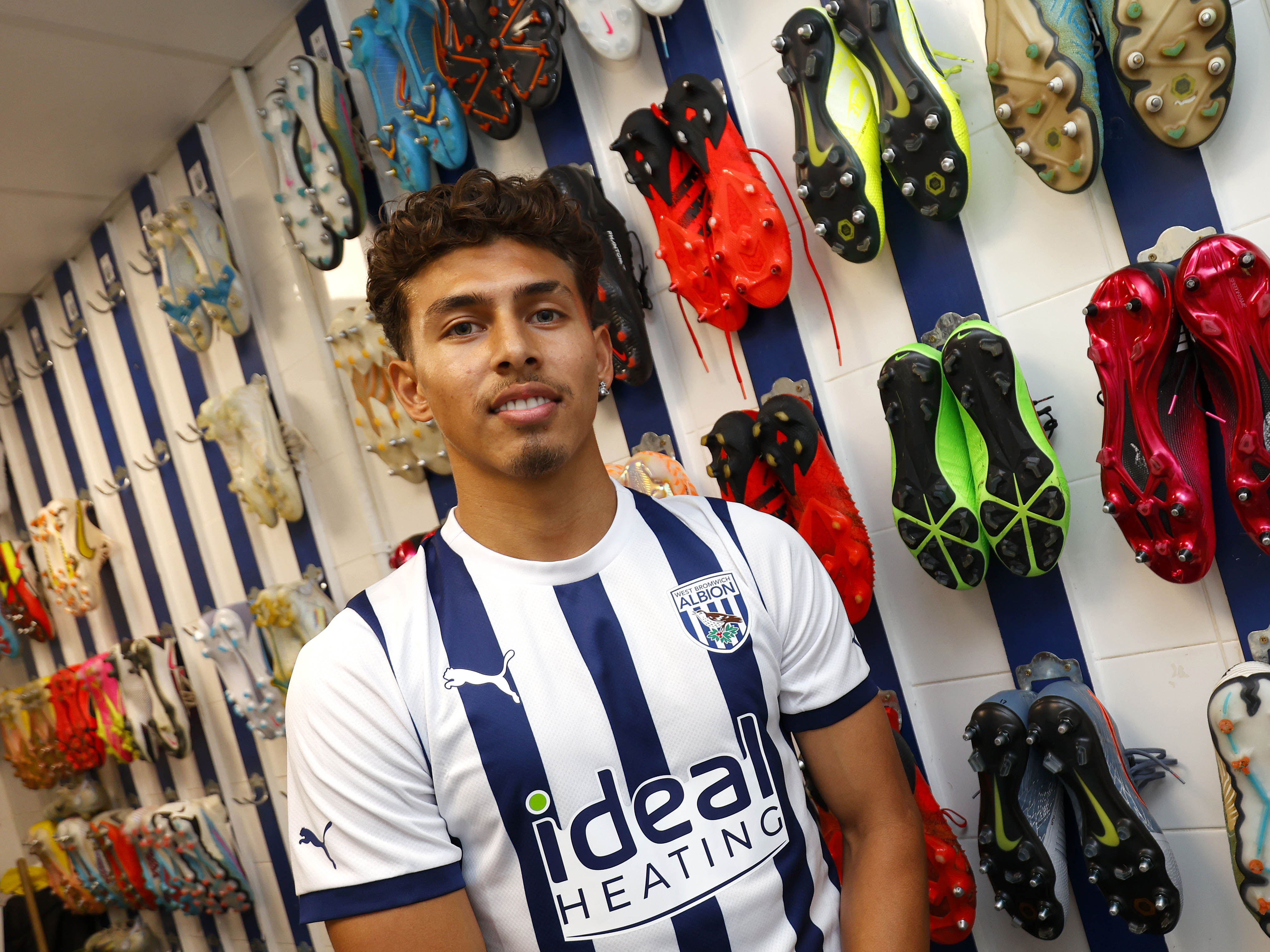 Jeremy Sarmiento smiles at the camera in the boot room wearing the home shirt