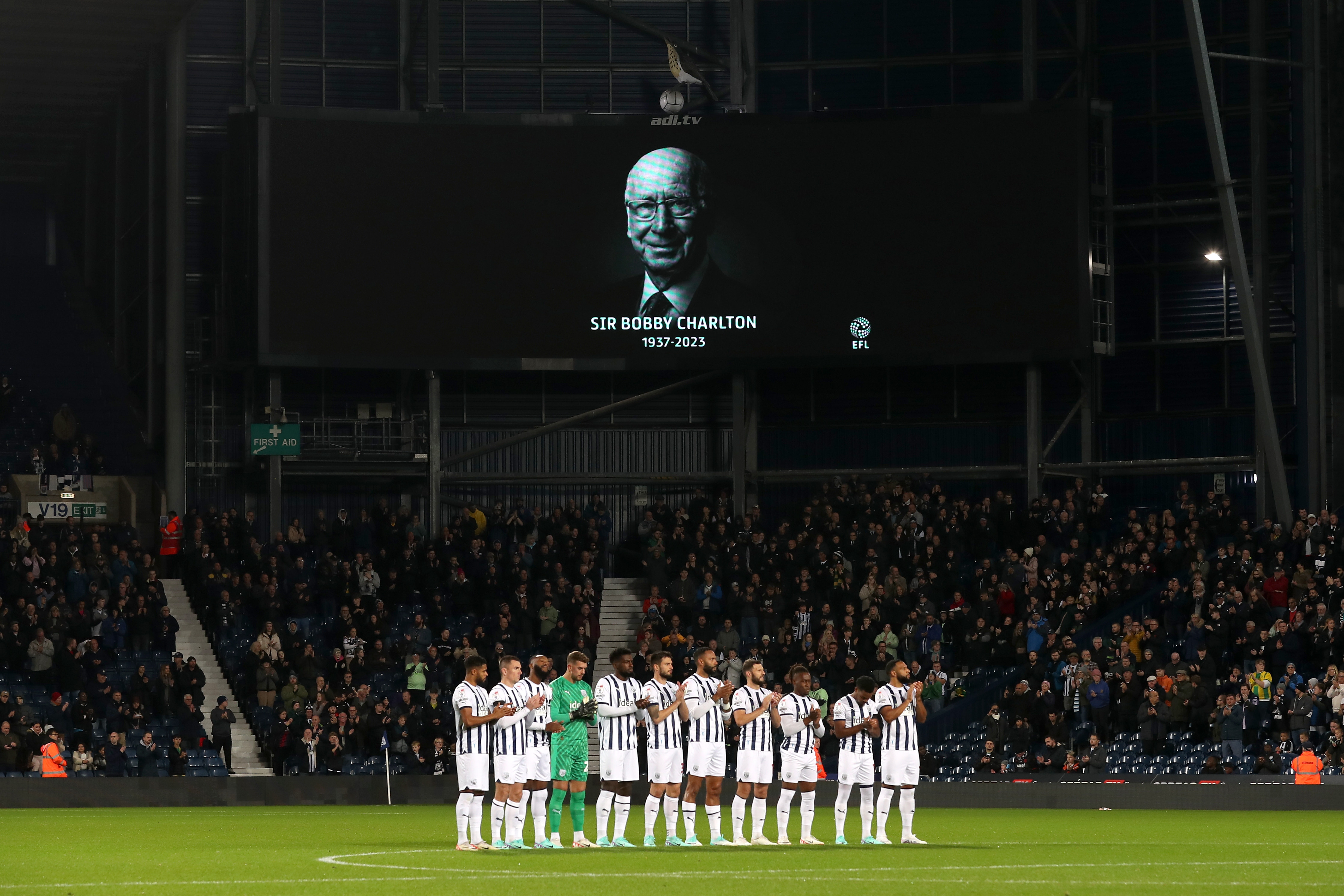 Albion players on the centre circle in a line with an image displayed of Sir Bobby Charlton behind them on the big screen