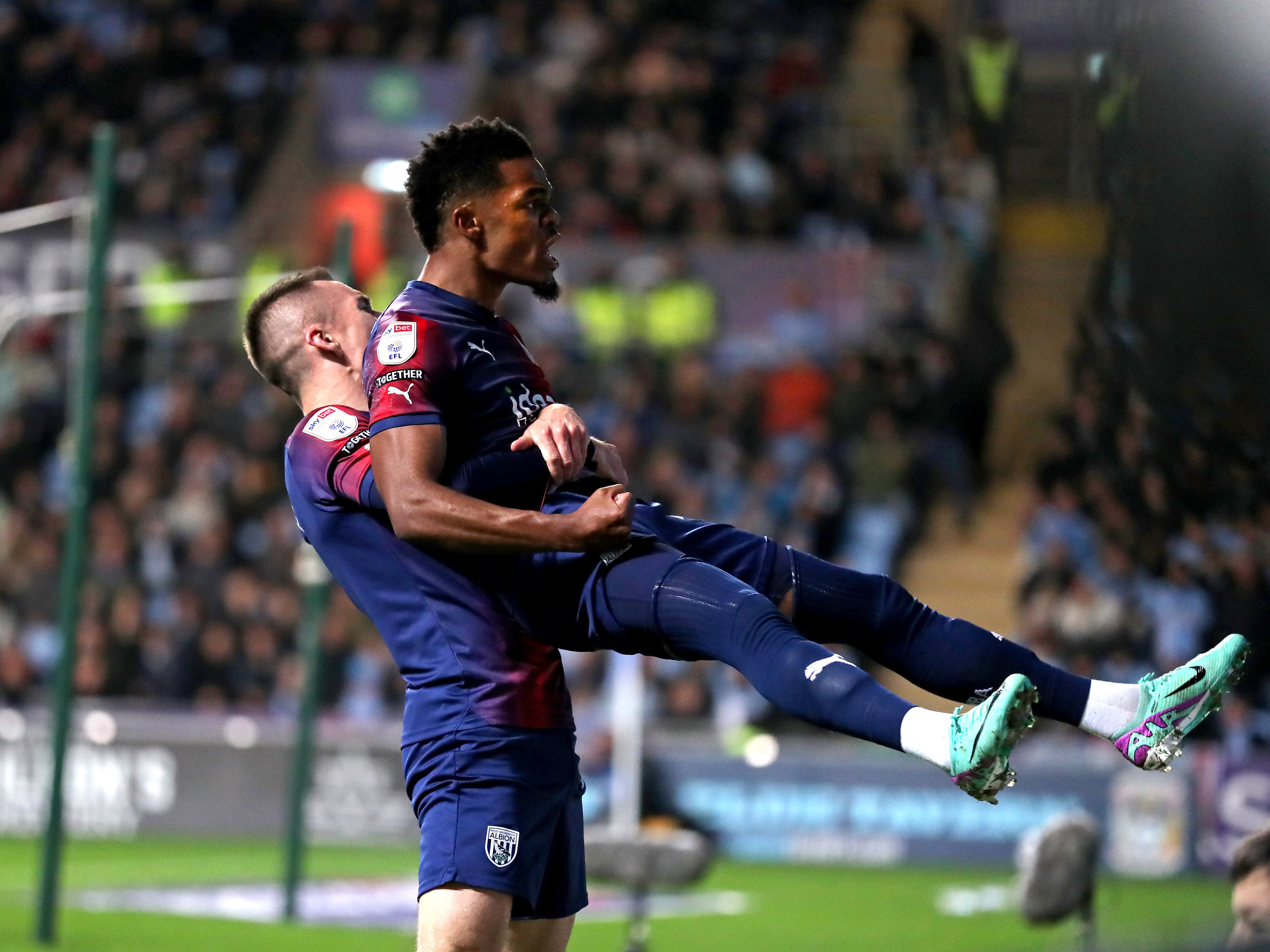 A photo of Grady Diangana, in the red and blue 2023/24 away colours, being lifted up by Jed Wallace after scoring v Coventry City at the CBS Arena