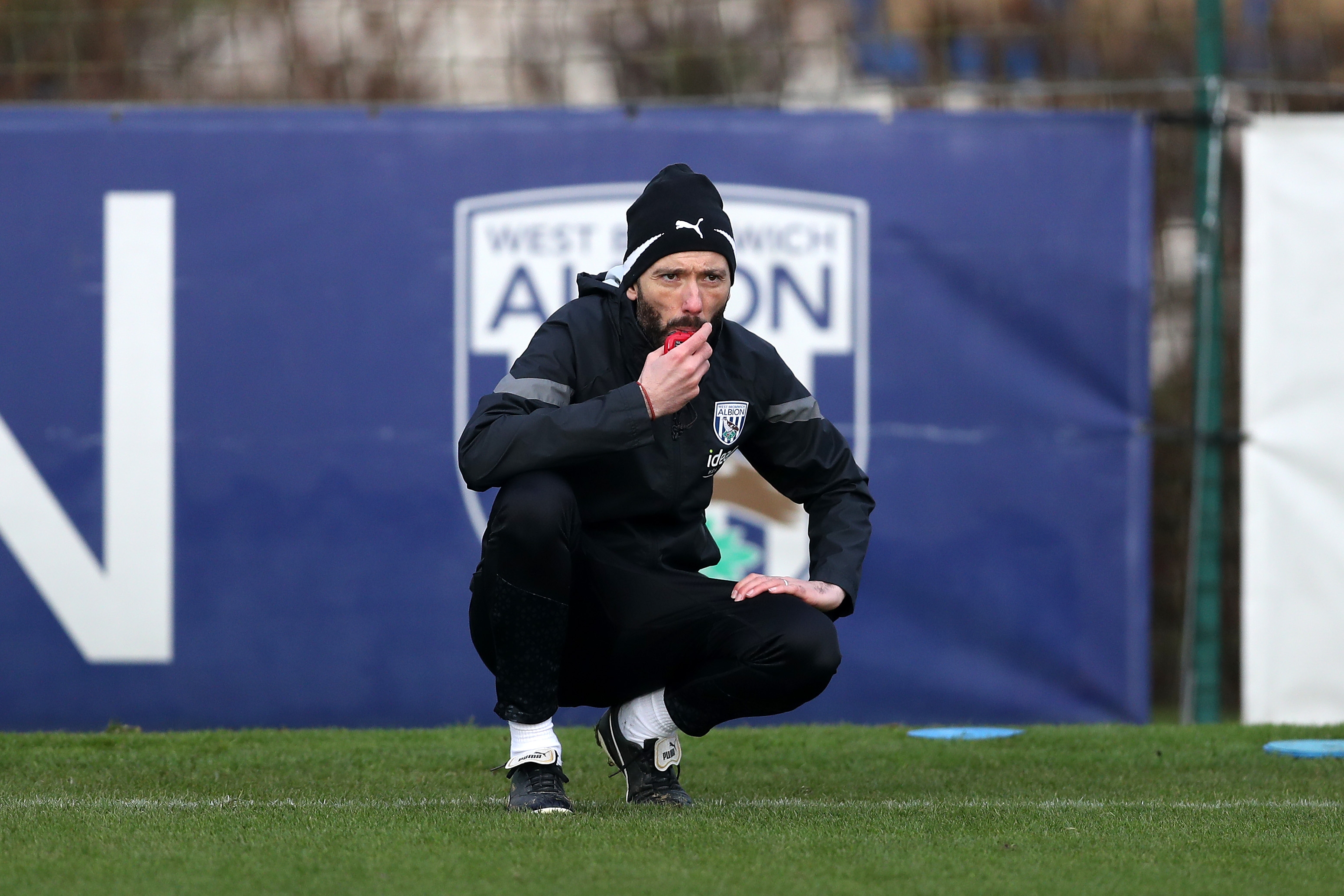 Carlos Corberán crouched down watching training in front of an Albion badge in the background