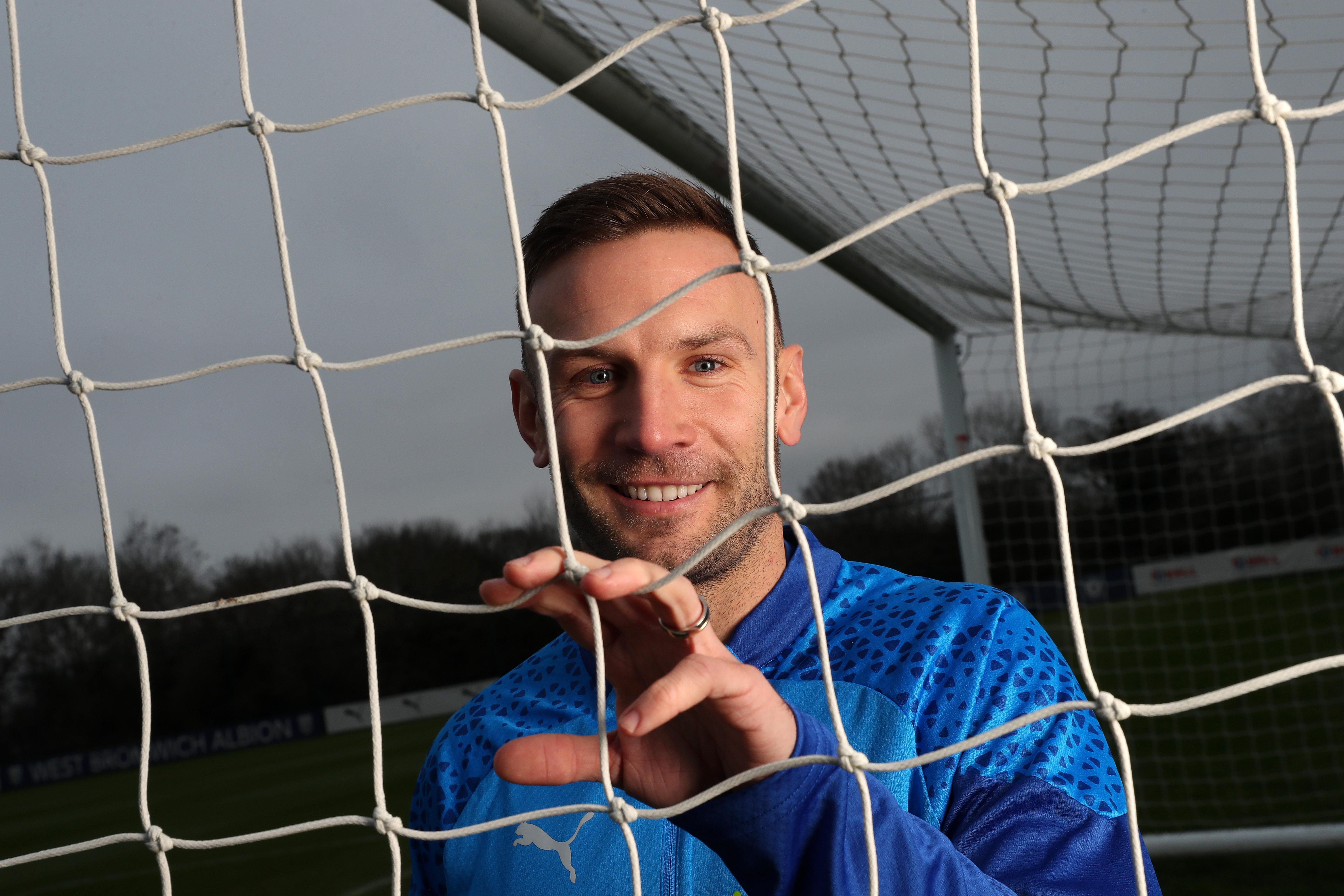 Andi Weimann smiling at the camera through a goal net