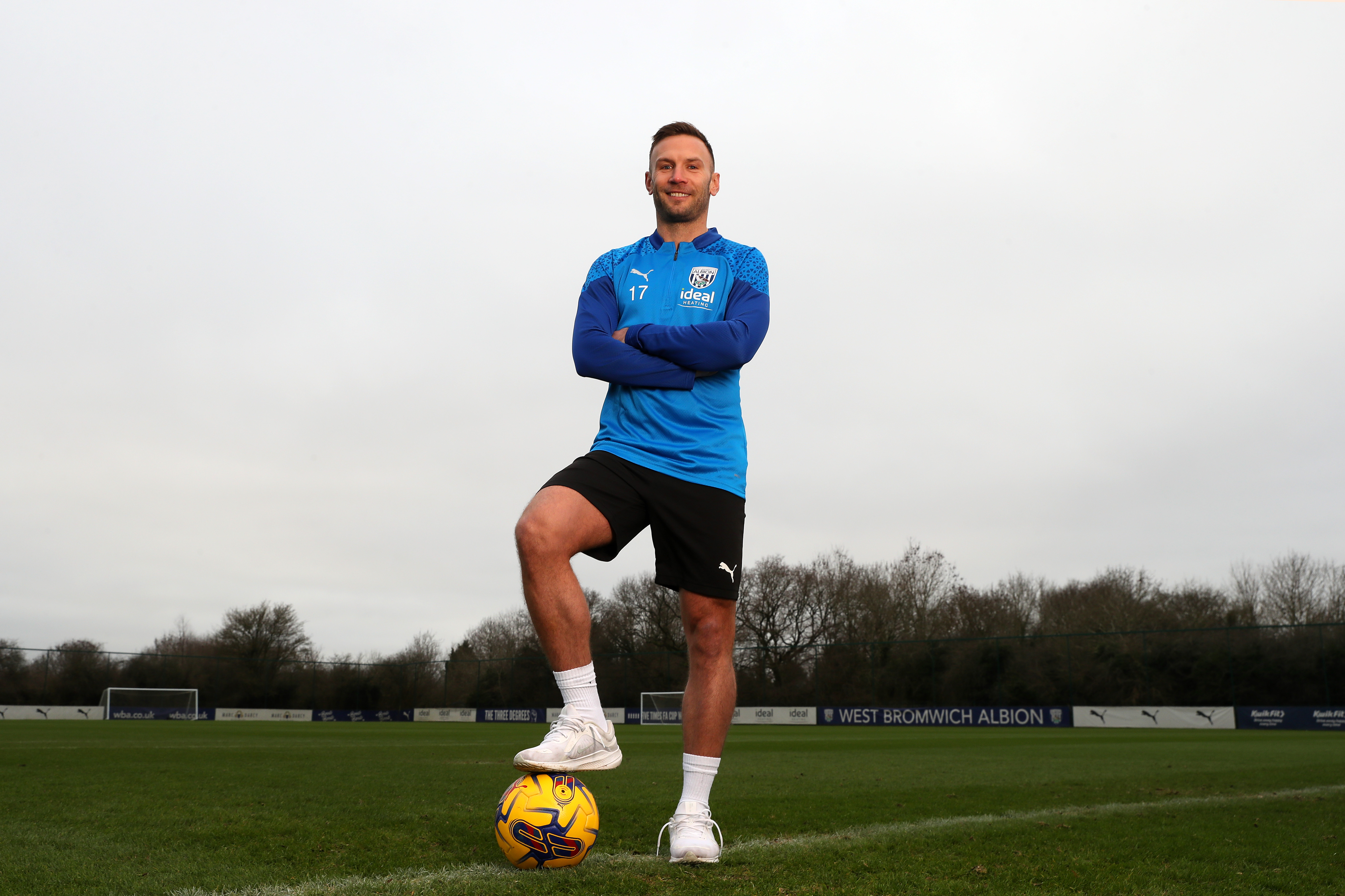 Andi Weimann smiling at the camera stood up with his foot on a ball and his arms folded