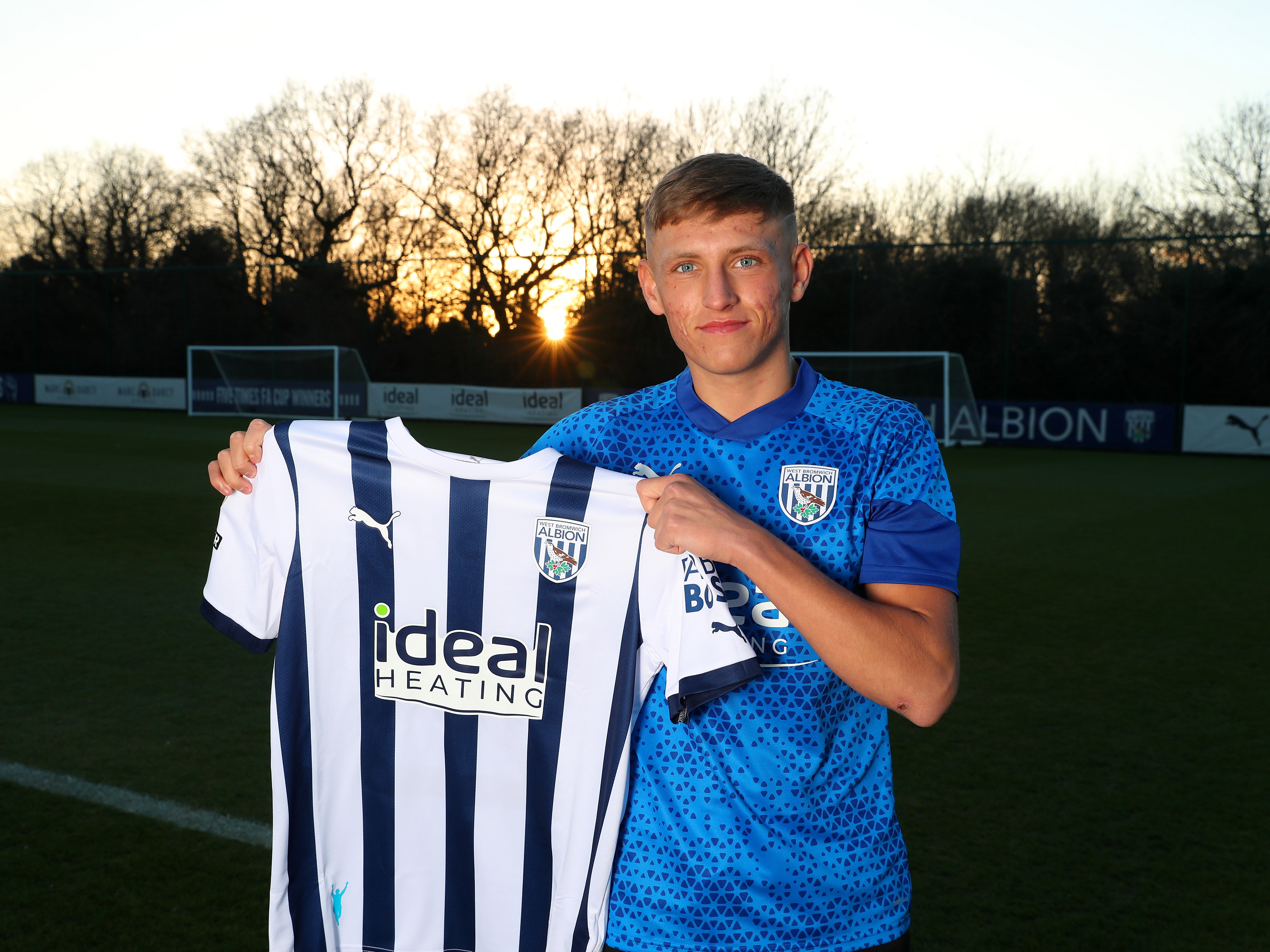 Callum Marshall holding up an Albion shirt while smiling at the camera