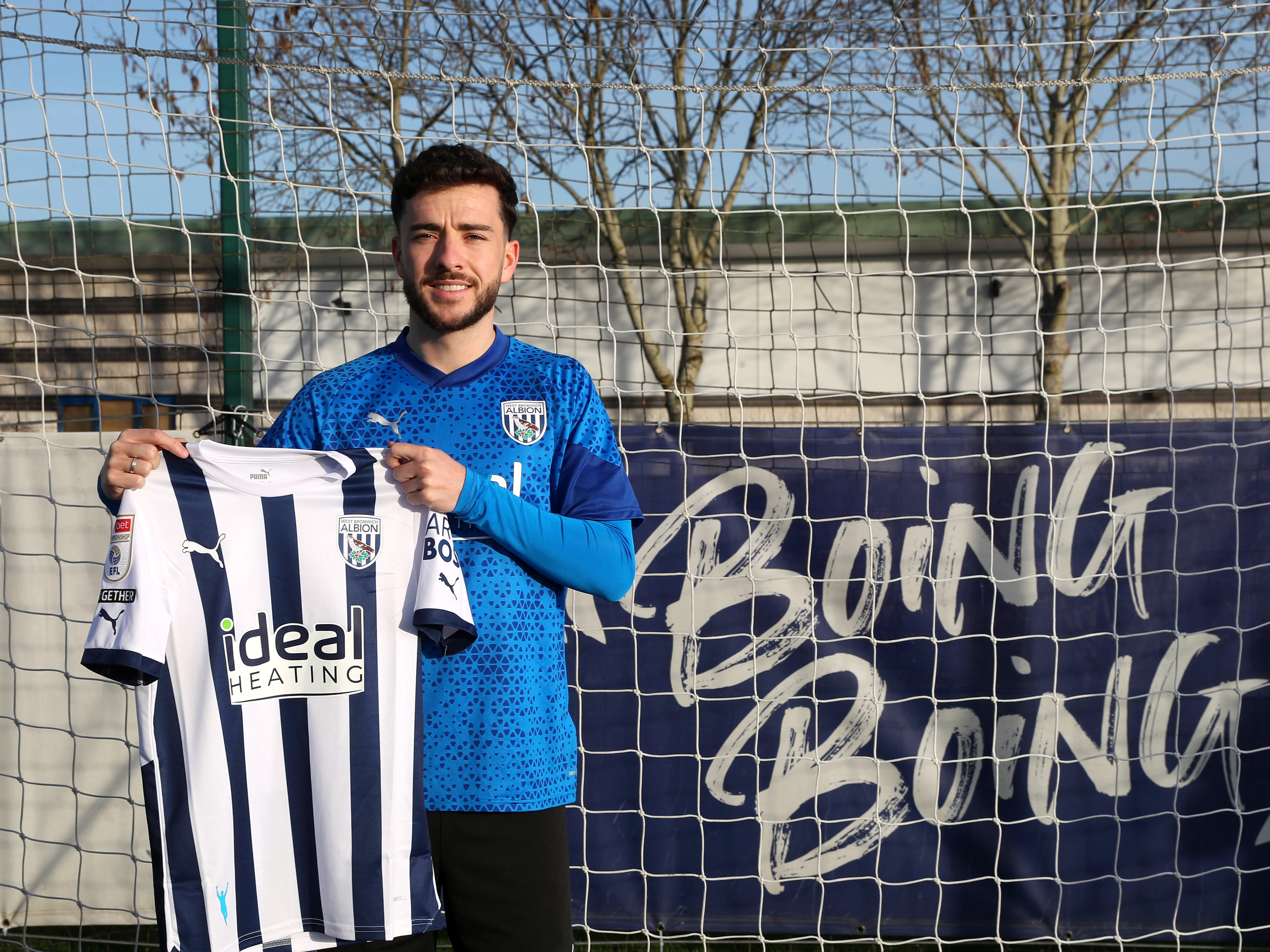 Mikey Johnstone posing for a photo in front of a 'Boing Boing' banner while holding up a home shirt