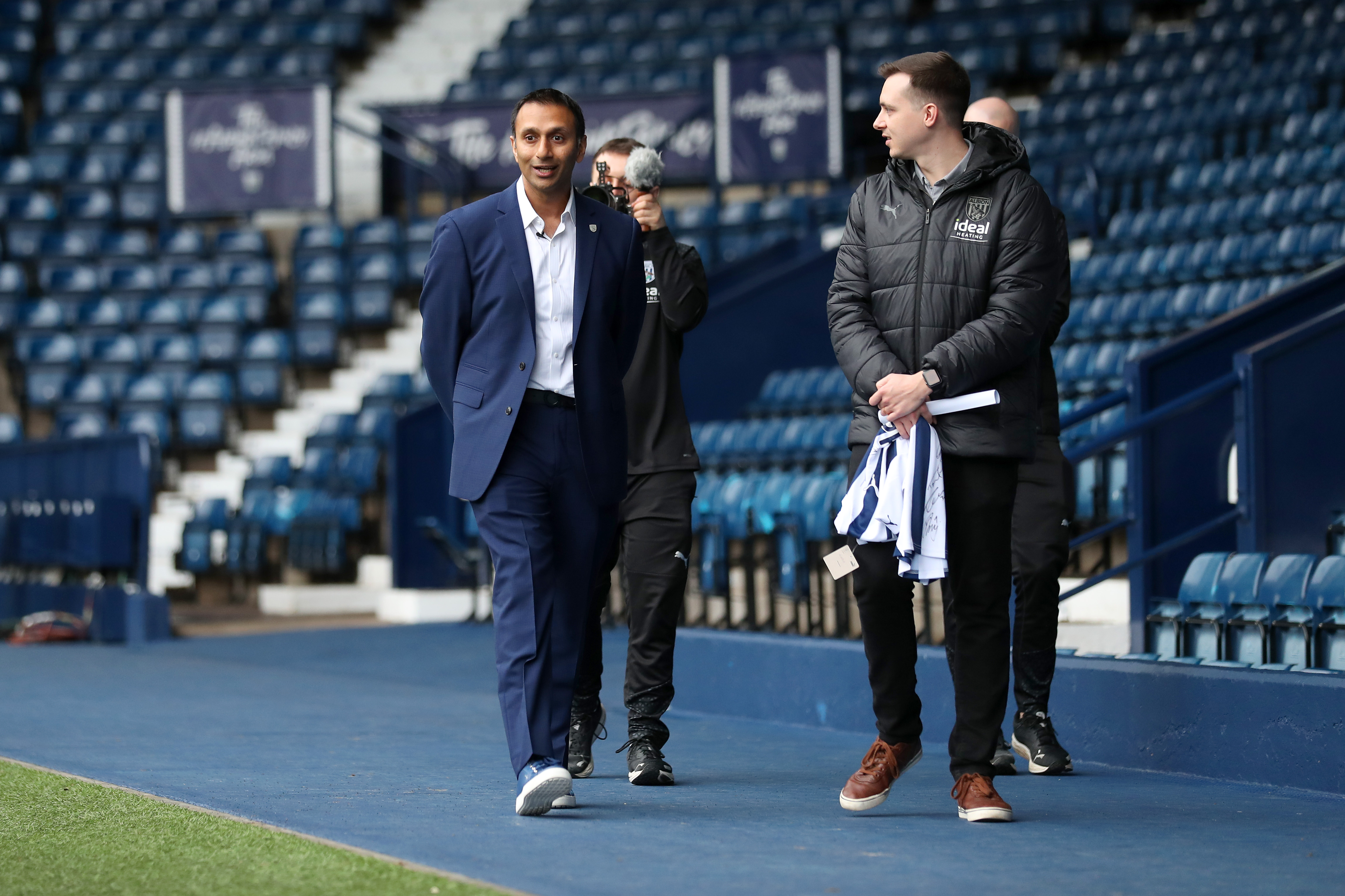 Shilen Patel walking along the blue track in front of the West Stand with West Bromwich Albion's Senior Communications Officer Sean Watts