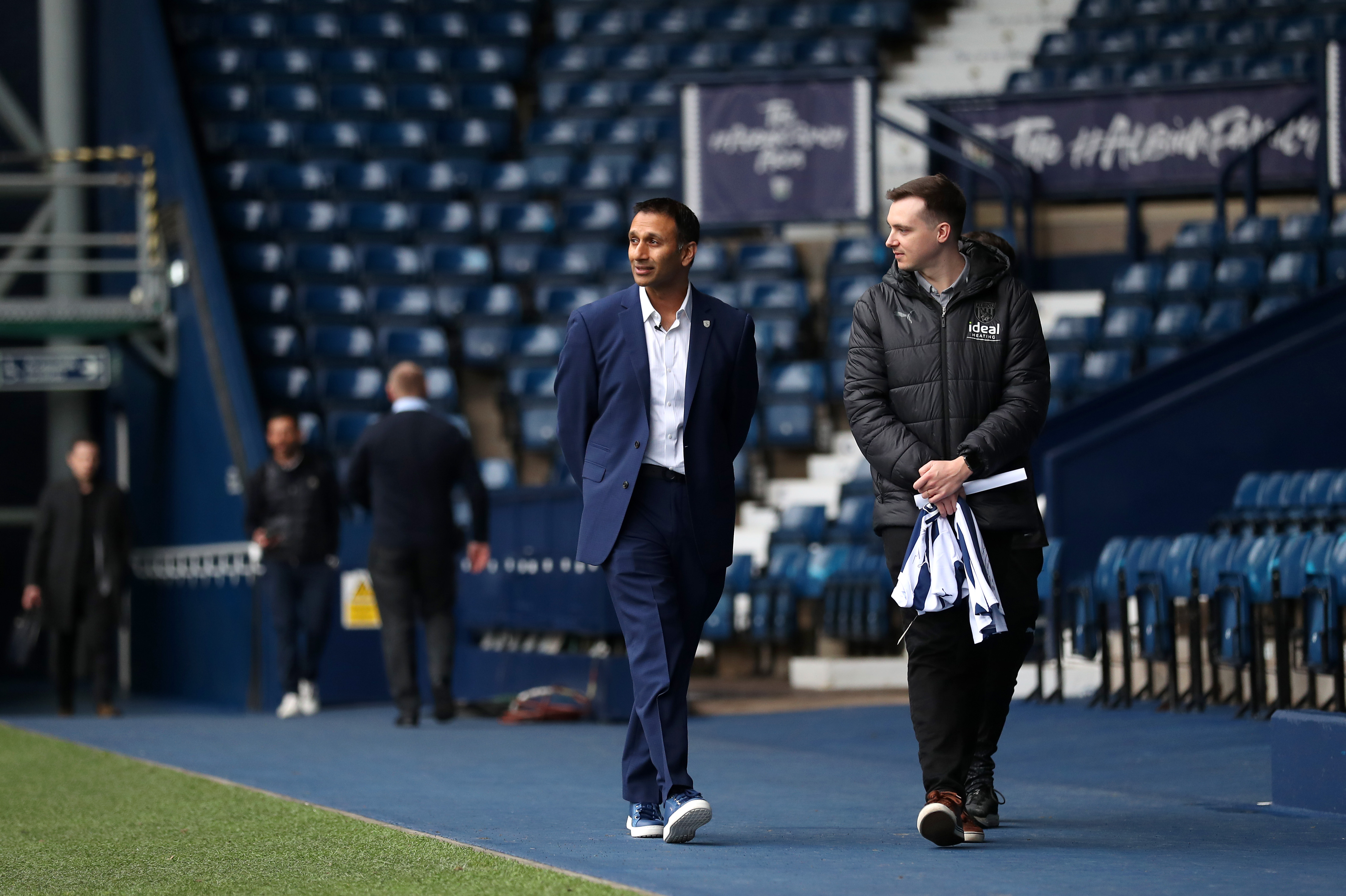 Shilen Patel walking along the blue track in front of the West Stand with West Bromwich Albion's Senior Communications Officer Sean Watts