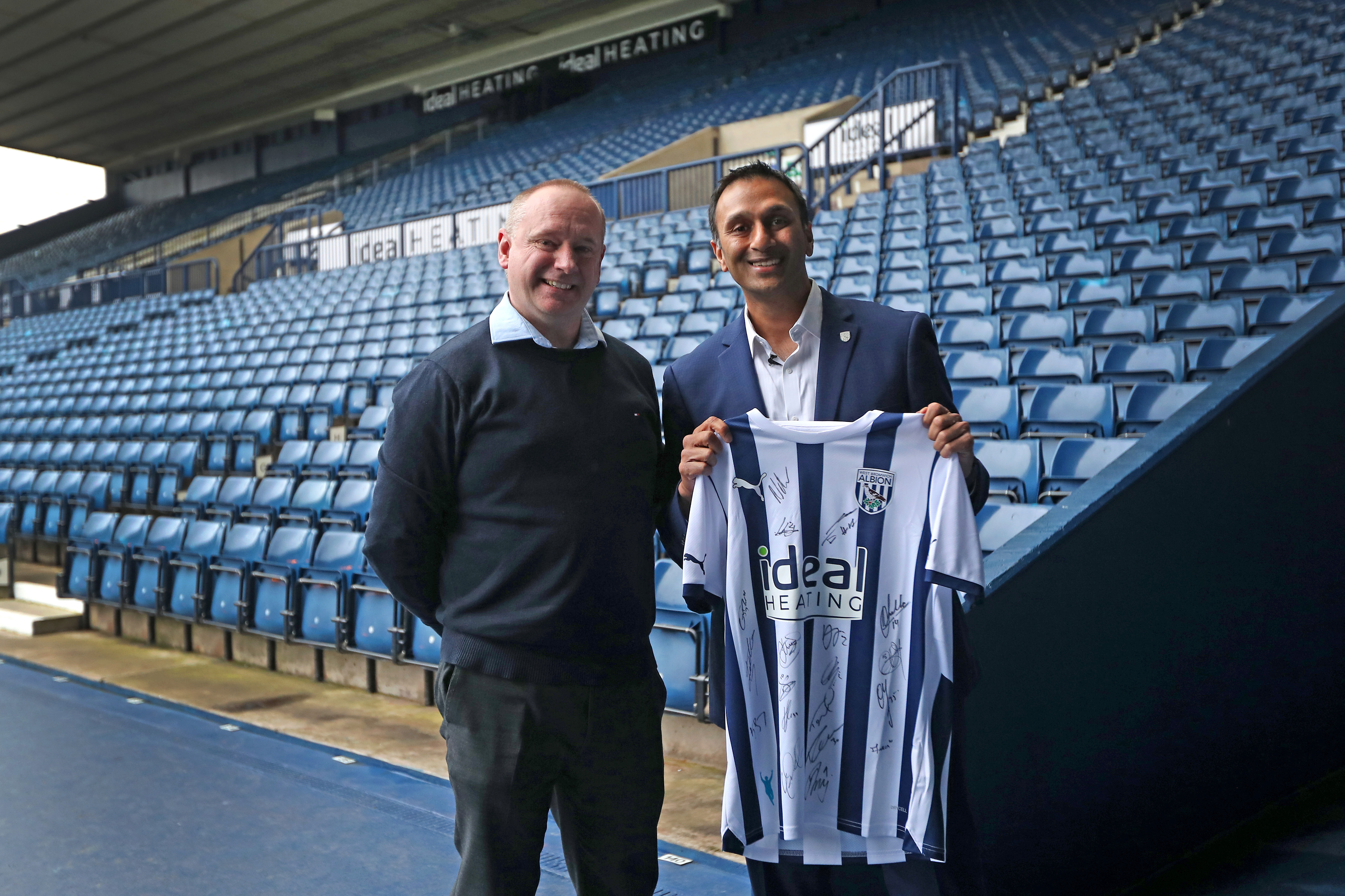 Shilen Patel poses for a photo with West Bromwich Albion's Managing Director Mark Miles while smiling and holding up a home Albion shirt