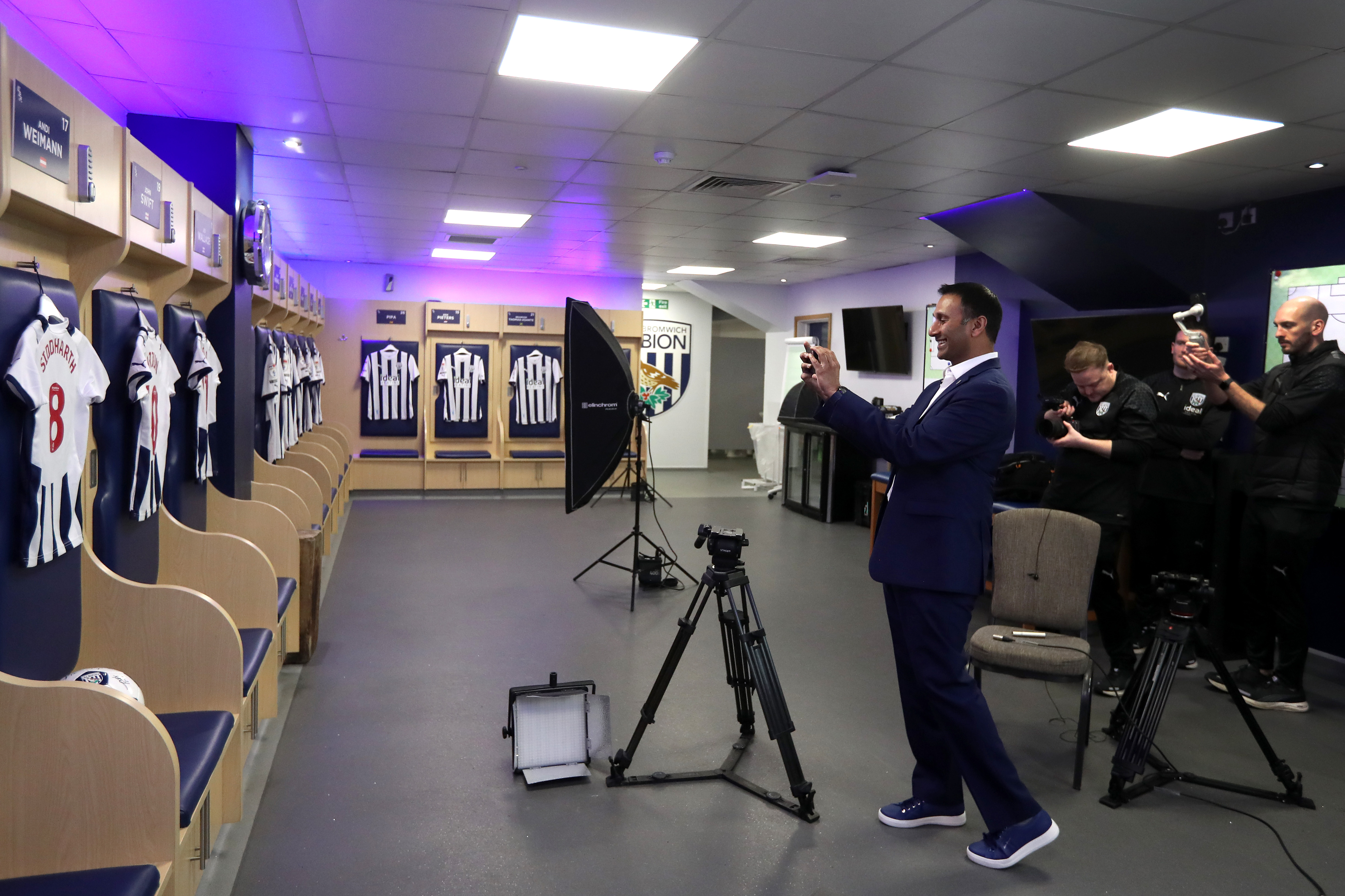 Shilen Patel taking a photo of Albion shirts on his phone in the home dressing room at The Hawthorns
