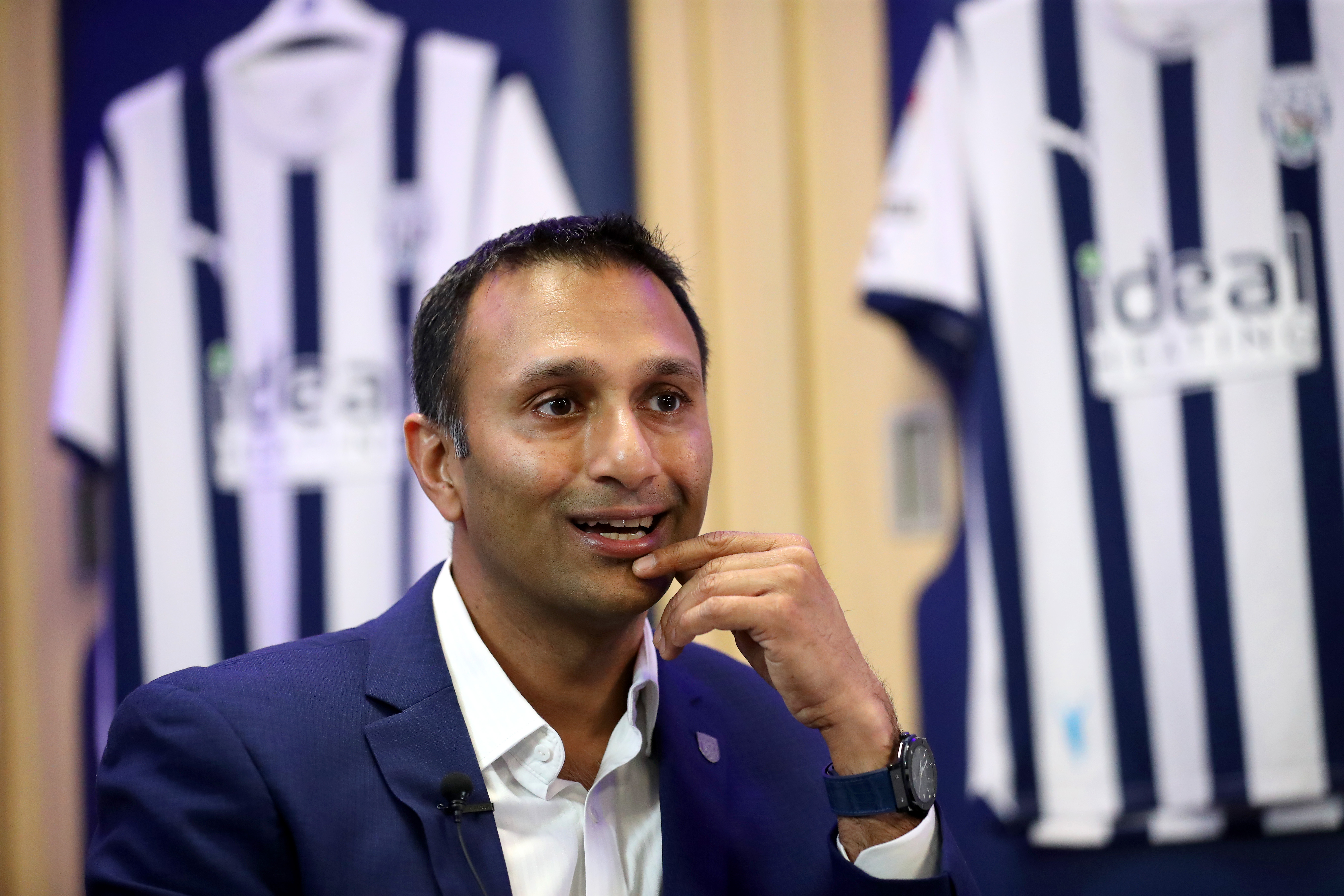 Shilen Patel is interviewed by WBA TV in the home dressing room with Albion shirts hanging behind him