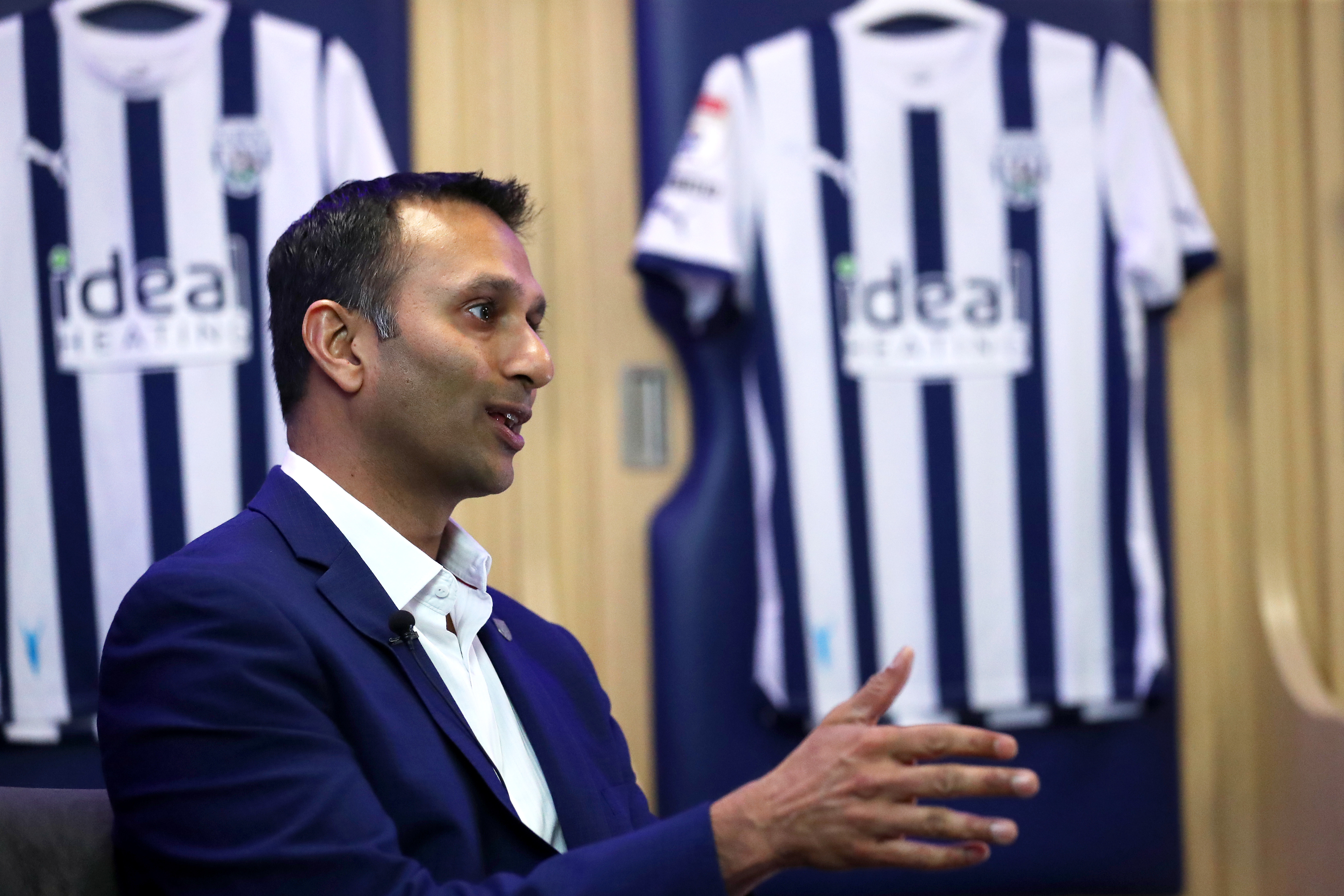 Shilen Patel is interviewed by WBA TV in the home dressing room with Albion shirts hanging behind him
