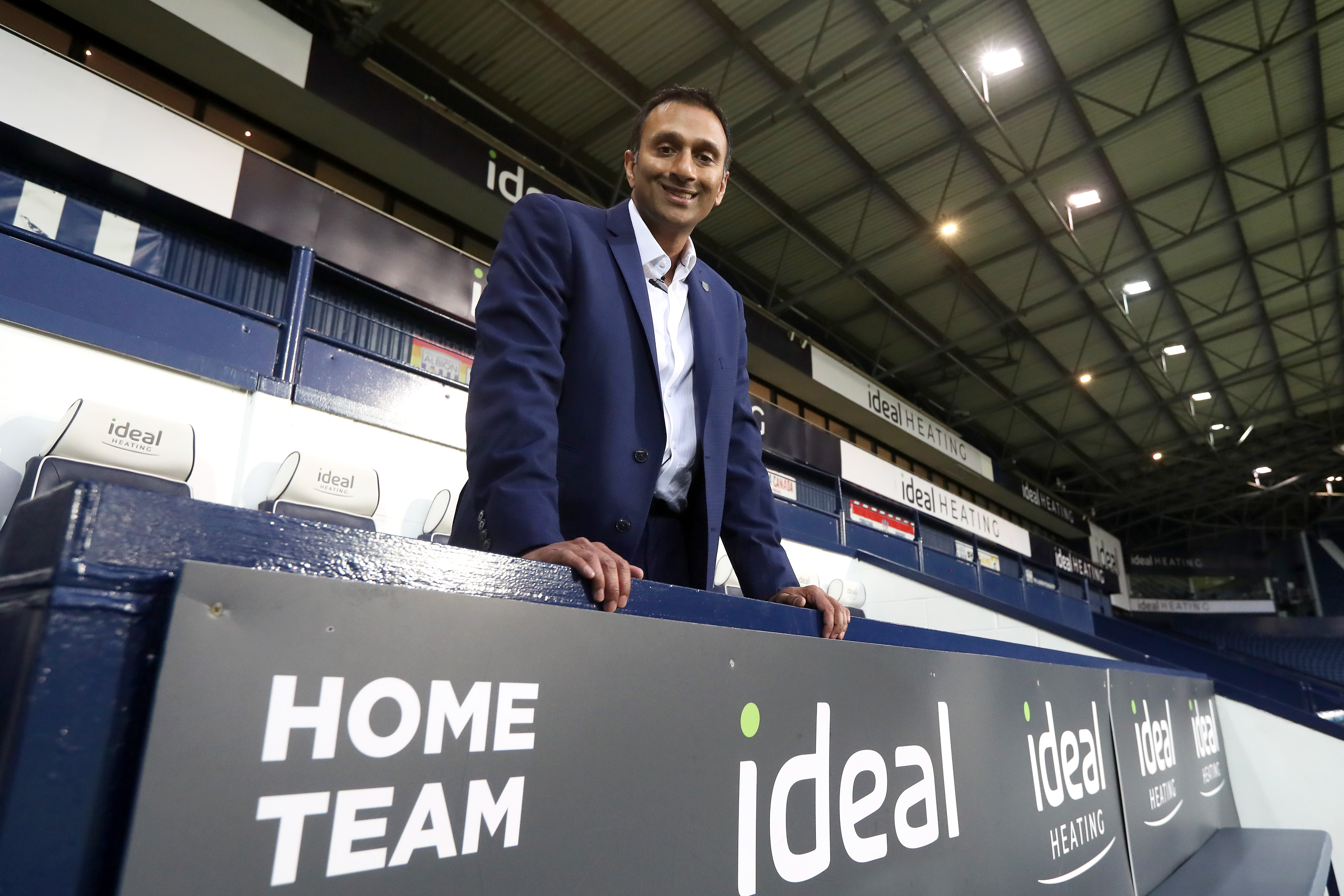 Shilen Patel stood in the home dugout at The Hawthorns in a suit smiling at the camera