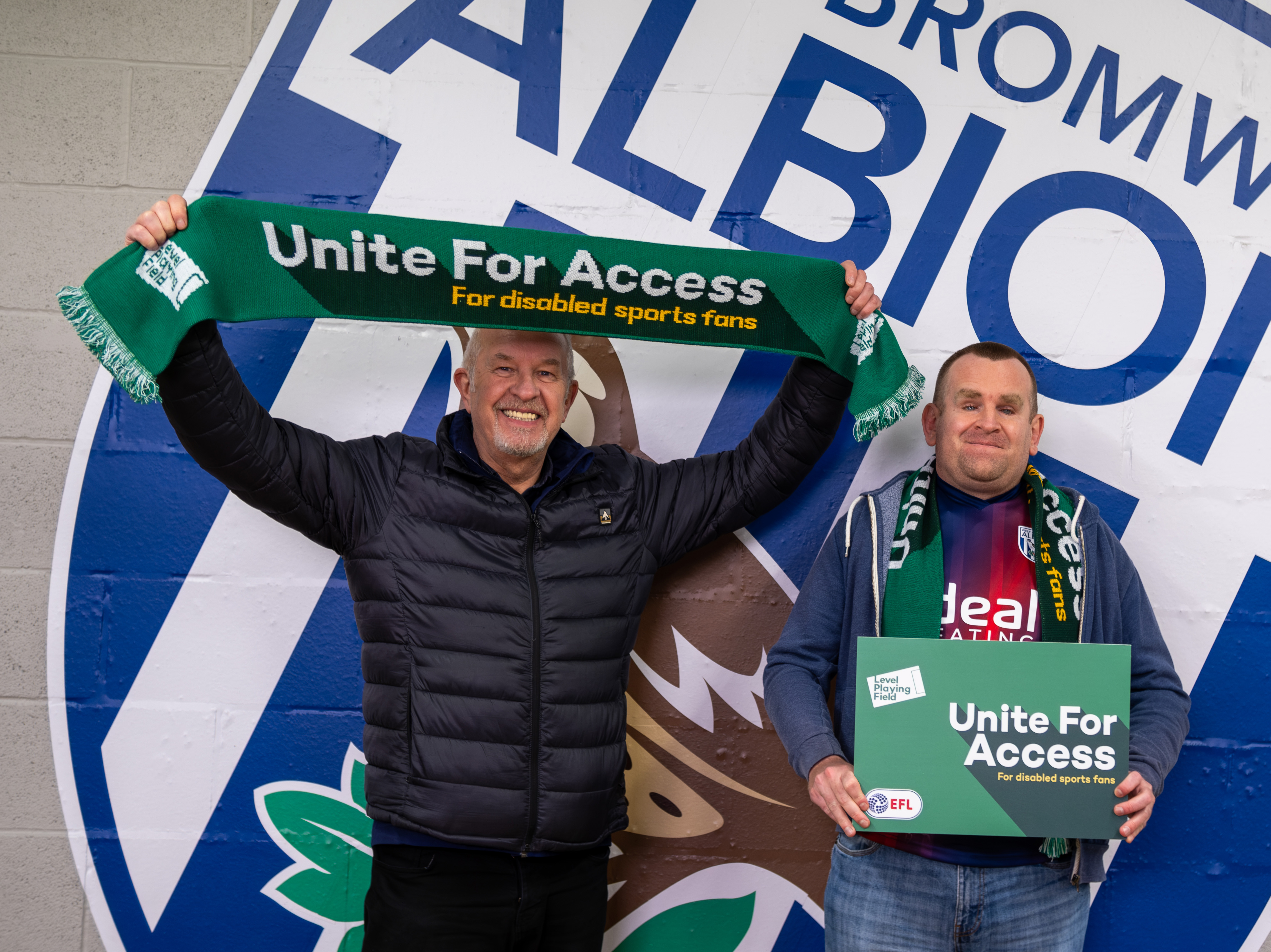West Bromwich Albion's Head of Health, Safety and Facilities Management Chris Harris and a Baggies fan holding up Level Playing Field branding while stood in front of a big Albion badge