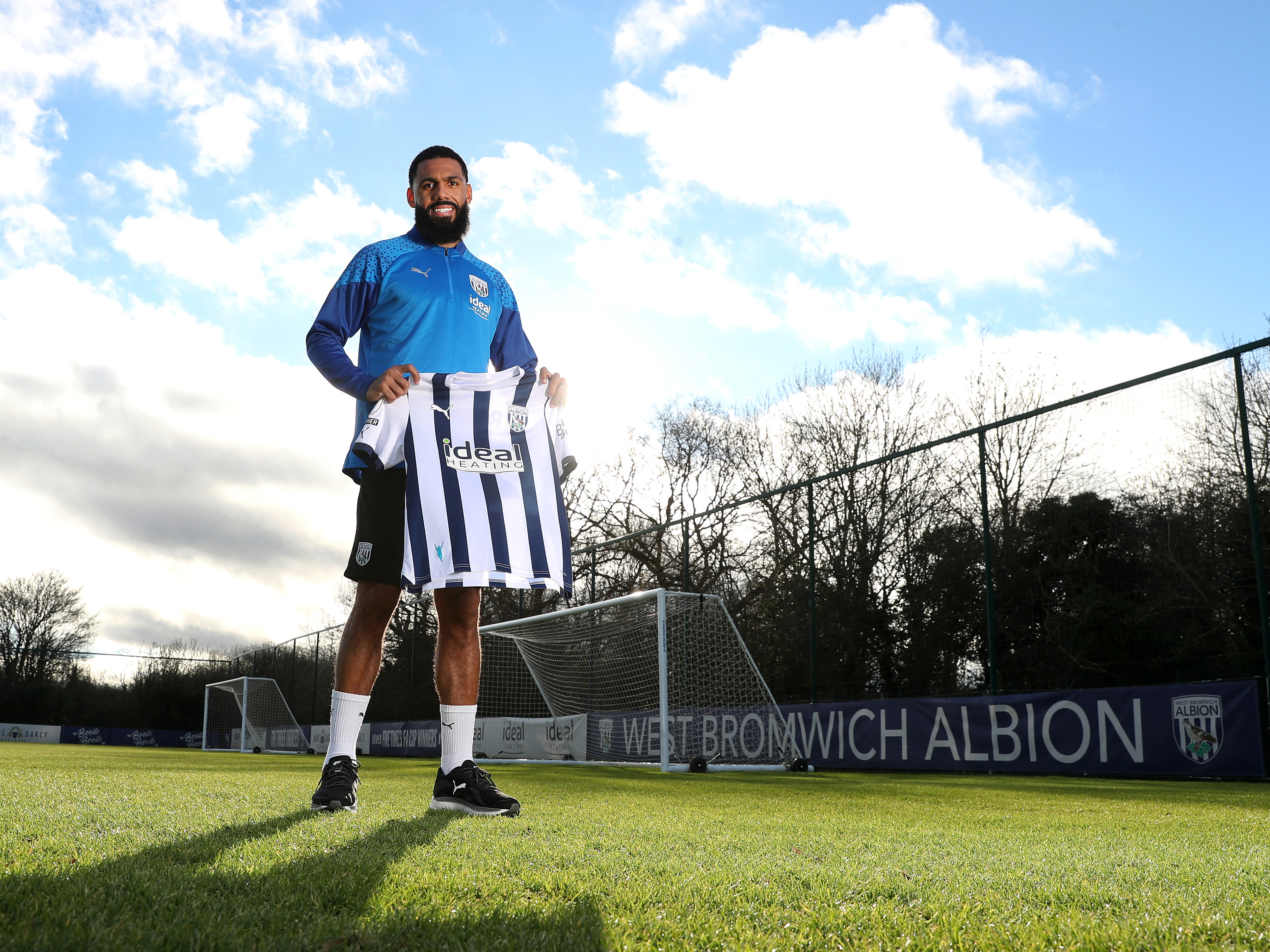 Yann M'Vila posing for a photo stood on the training pitch while holding a home shirt
