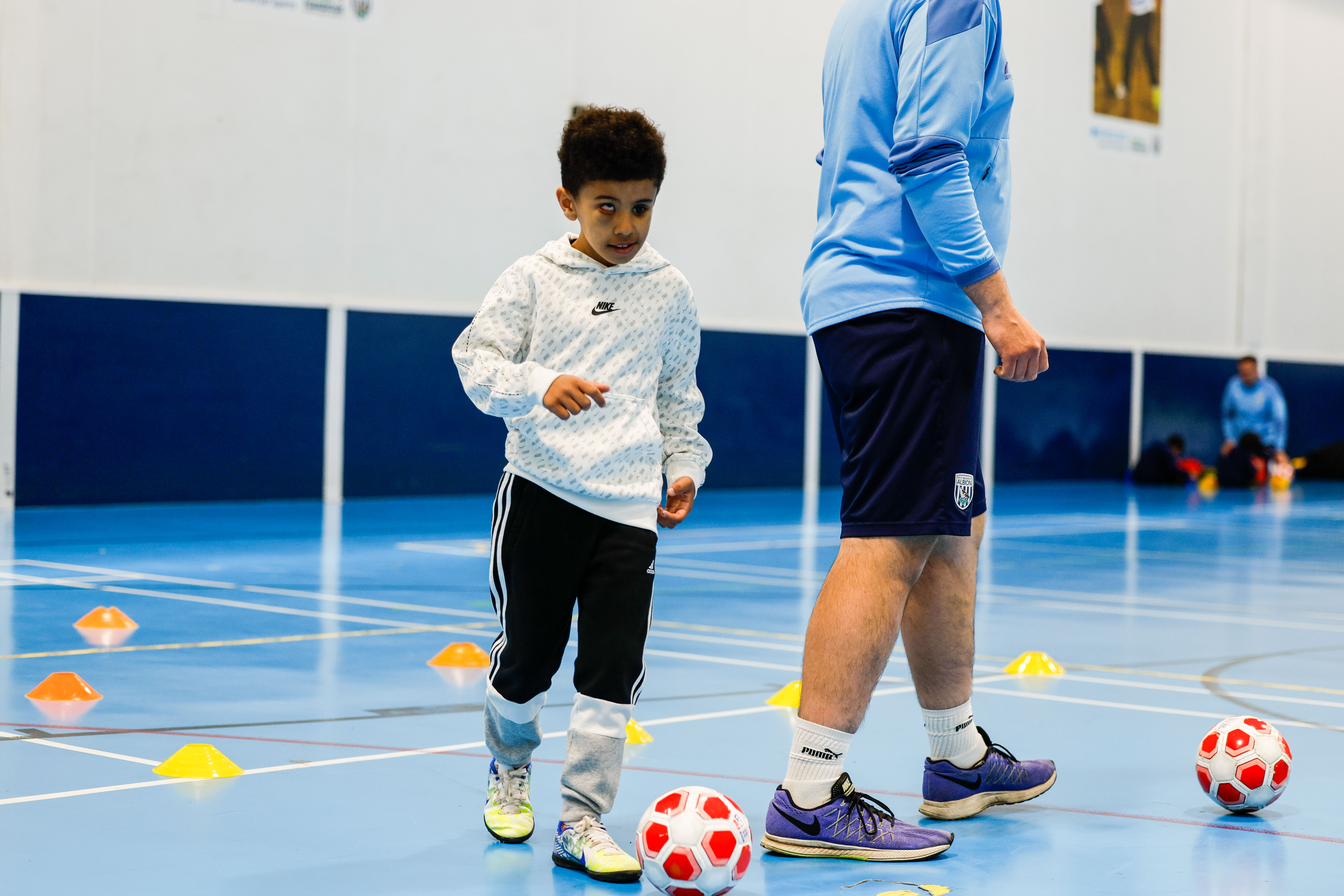 Young visually impaired player with the ball at this feet, a Foundation coach standing behind to the right.