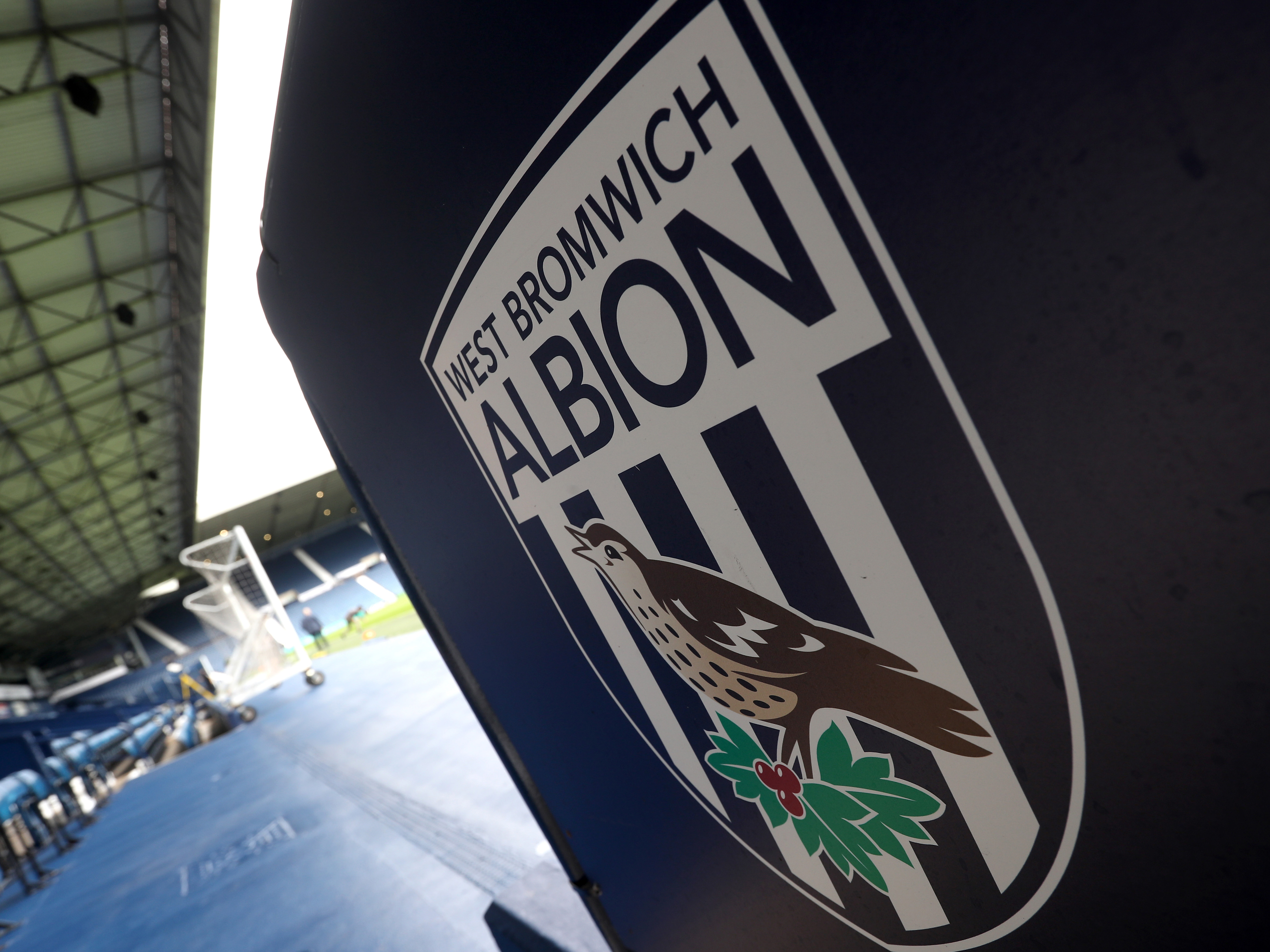 An Albion badge with the inside of The Hawthorns in the background 