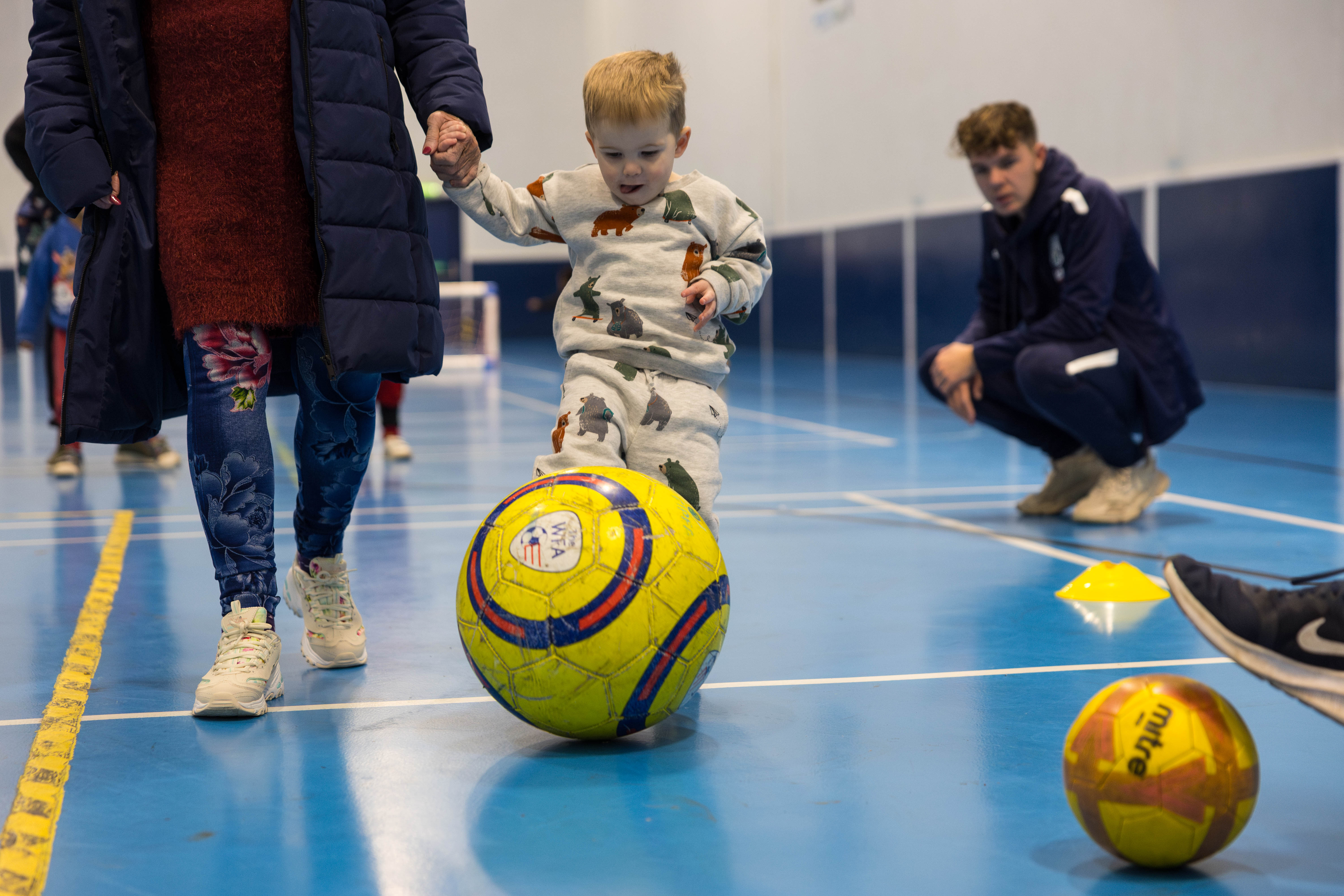 Mini Baggies participant kicking a ball while being coached by a TAF coach