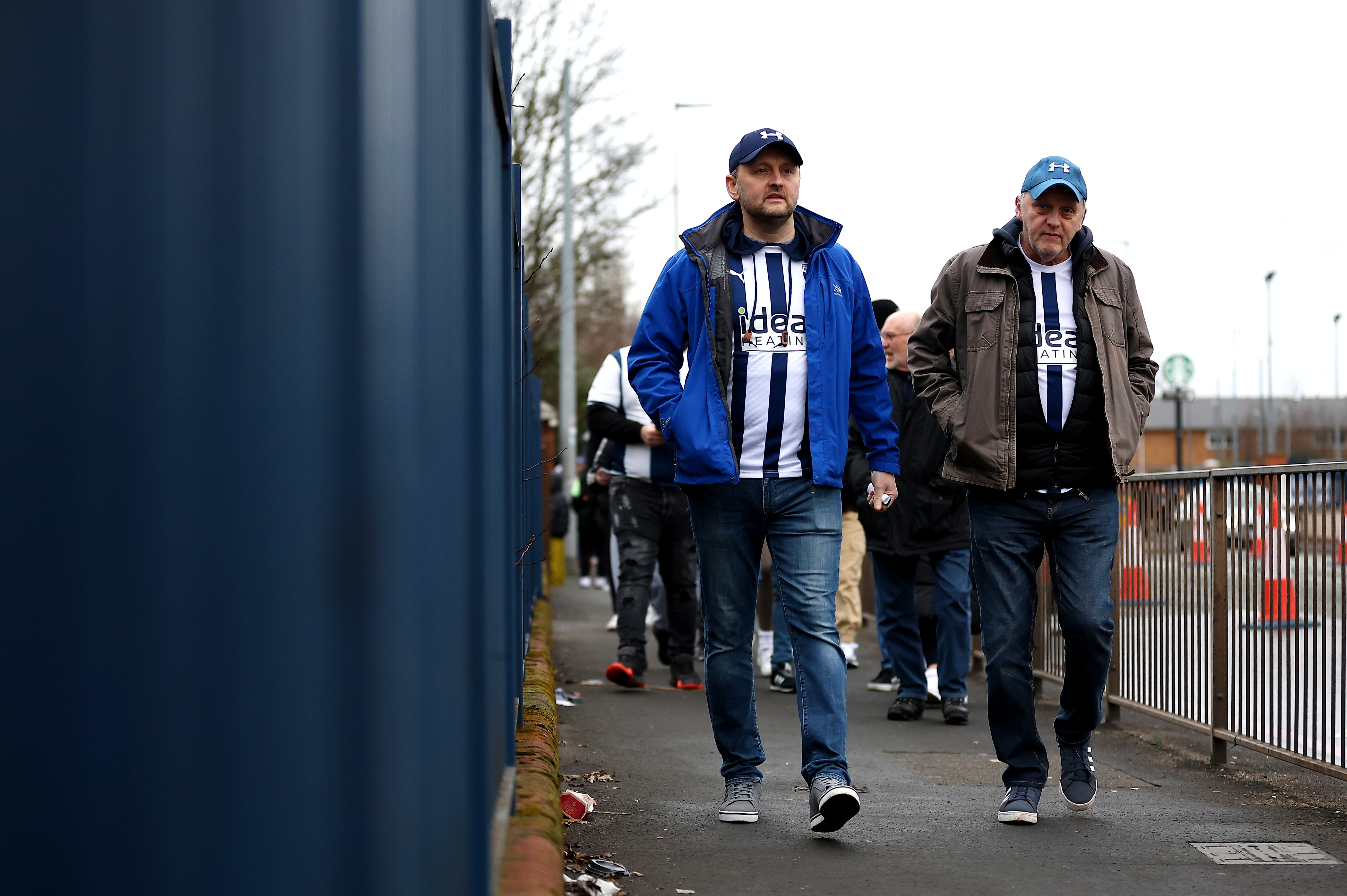 Two male Albion supporters walk towards The Hawthorns while wearing home shirts