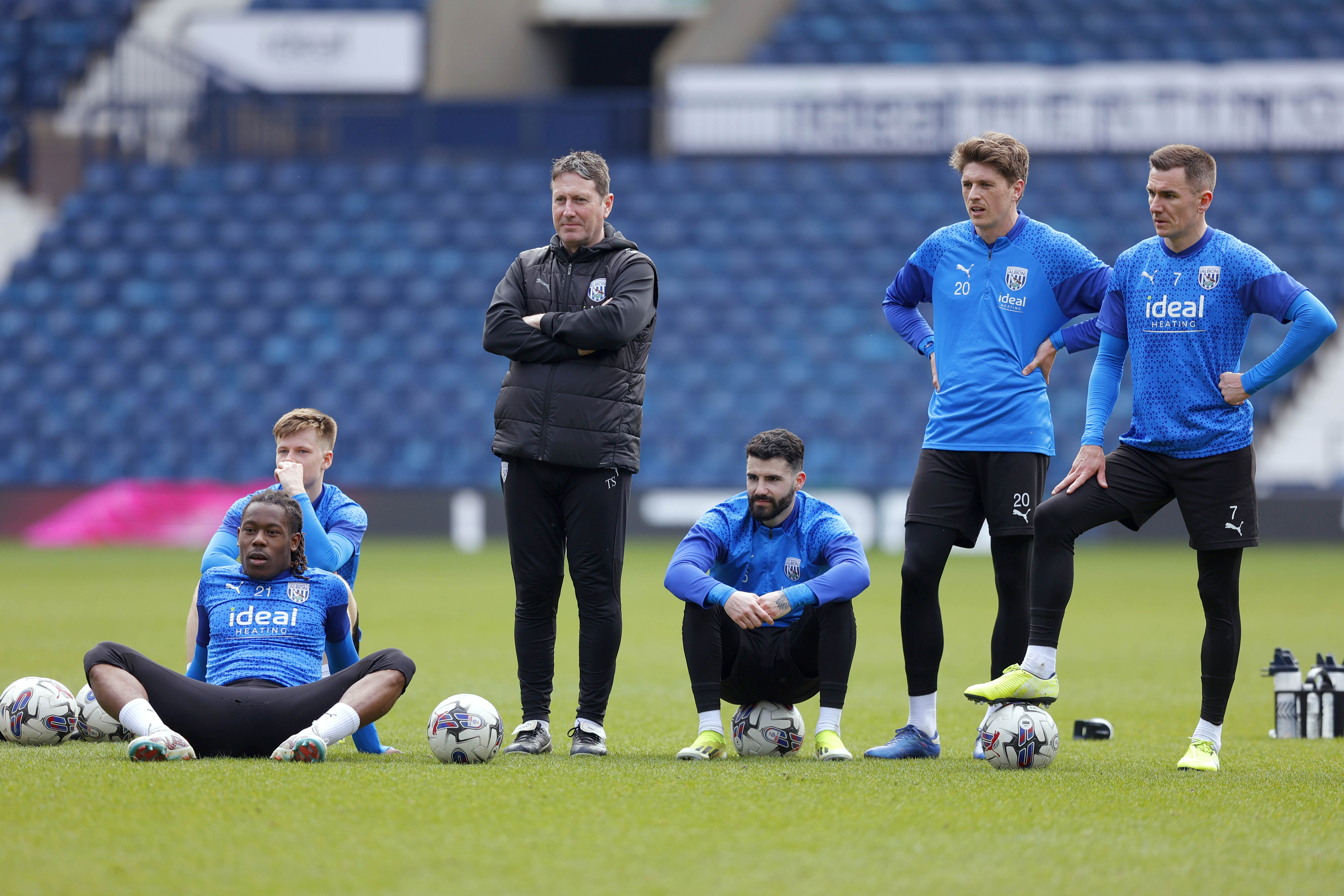 Some Albion players sit on the floor while others stand and watch during a pause in the session at The Hawthorns