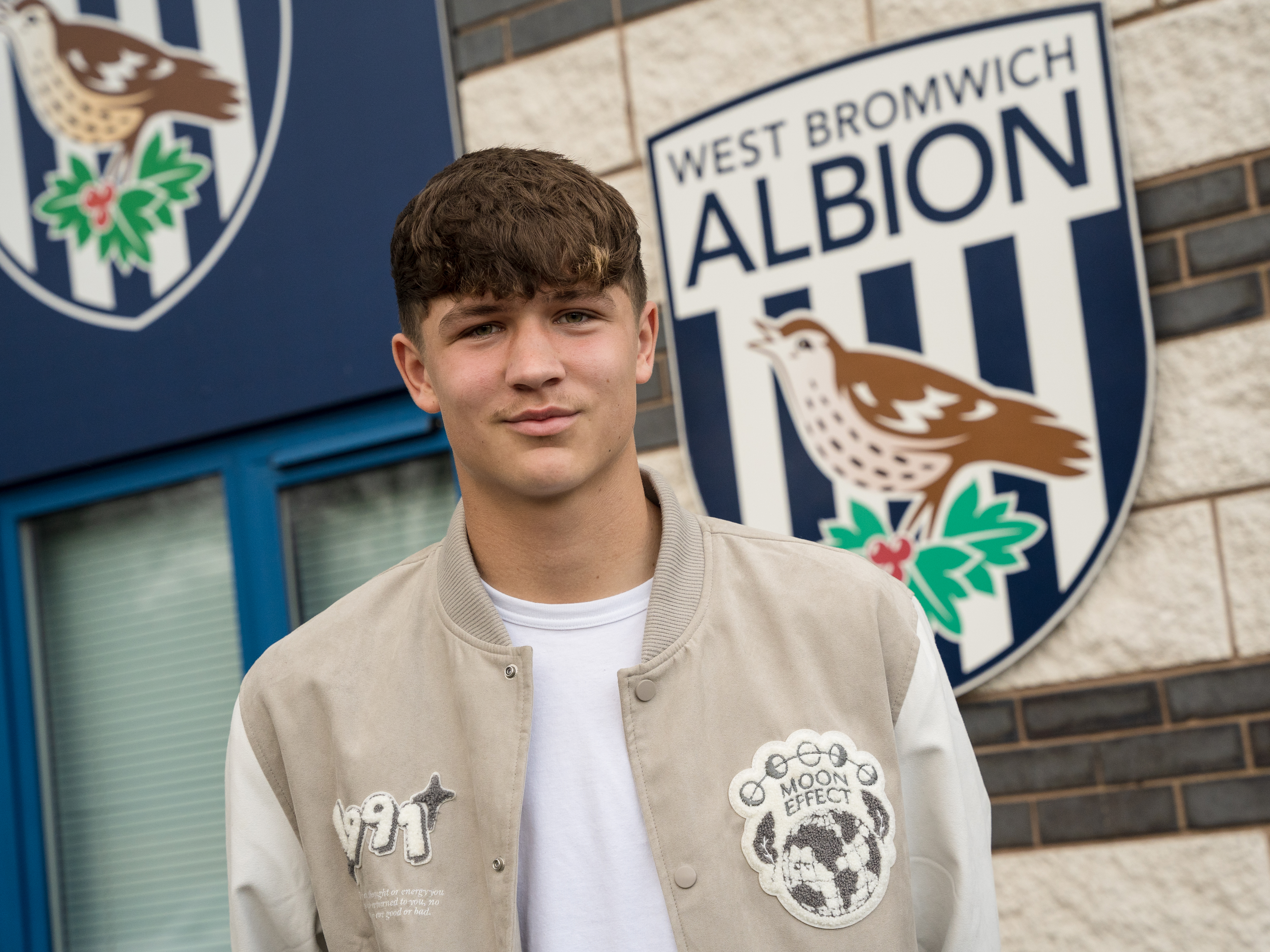 A photo of Albion youngster Cole Deeming in front of the Albion badge at the training ground