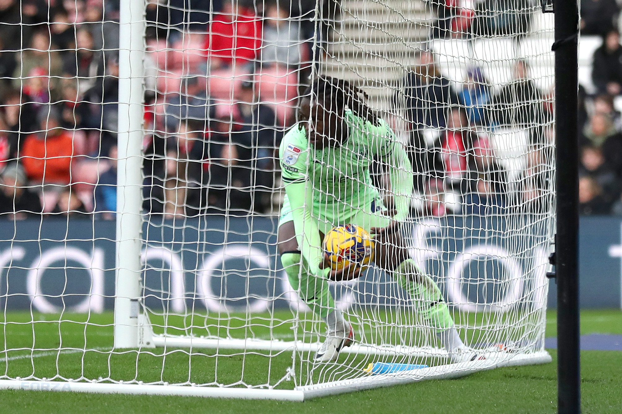 Brandon Thomas-Asante picking the ball out of the back of the net at the Stadium of Light after scoring against Sunderland while wearing the lime green away kit