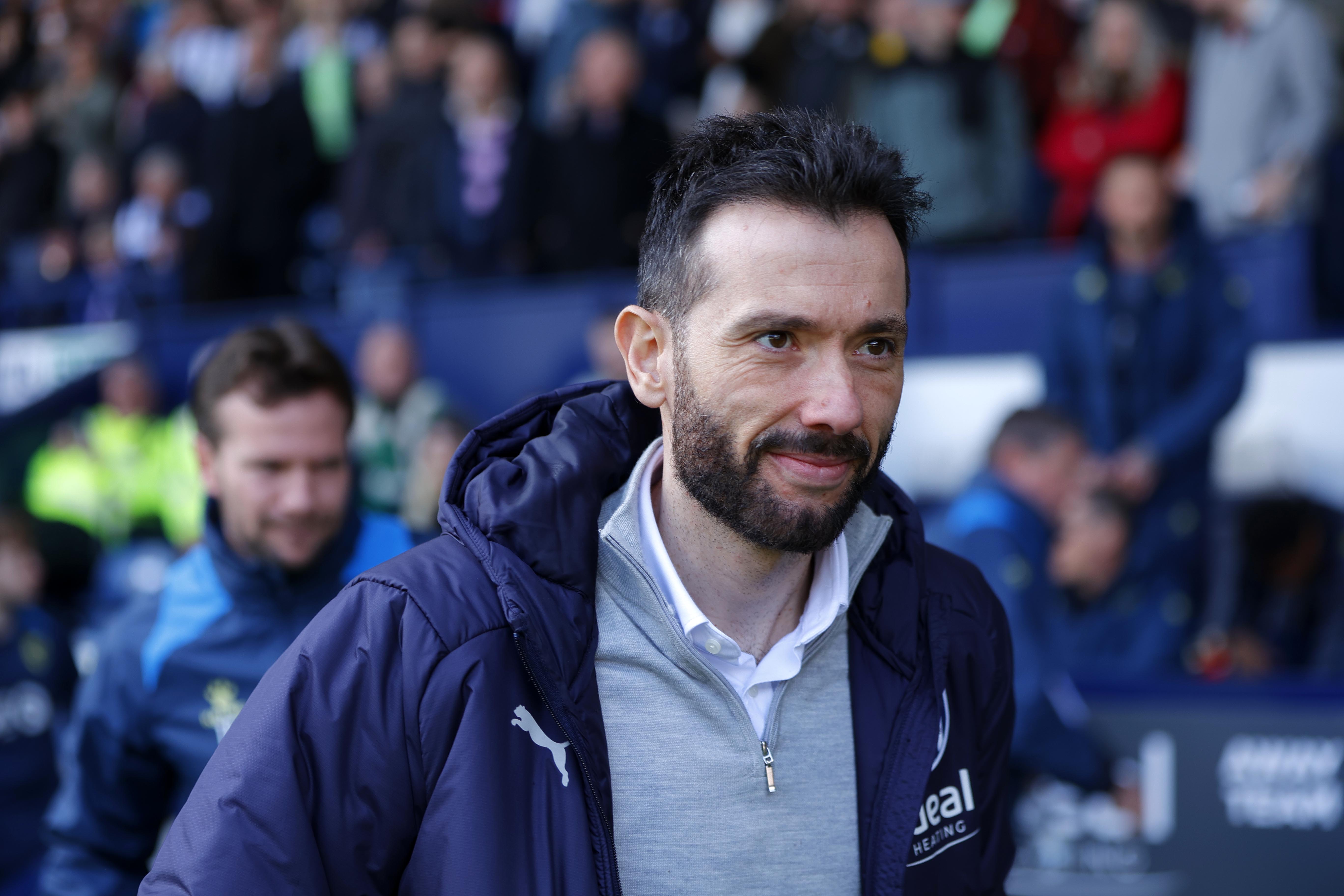 Carlos Corberán smiling before a game on the side of the pitch at The Hawthorns wearing an Albion coat
