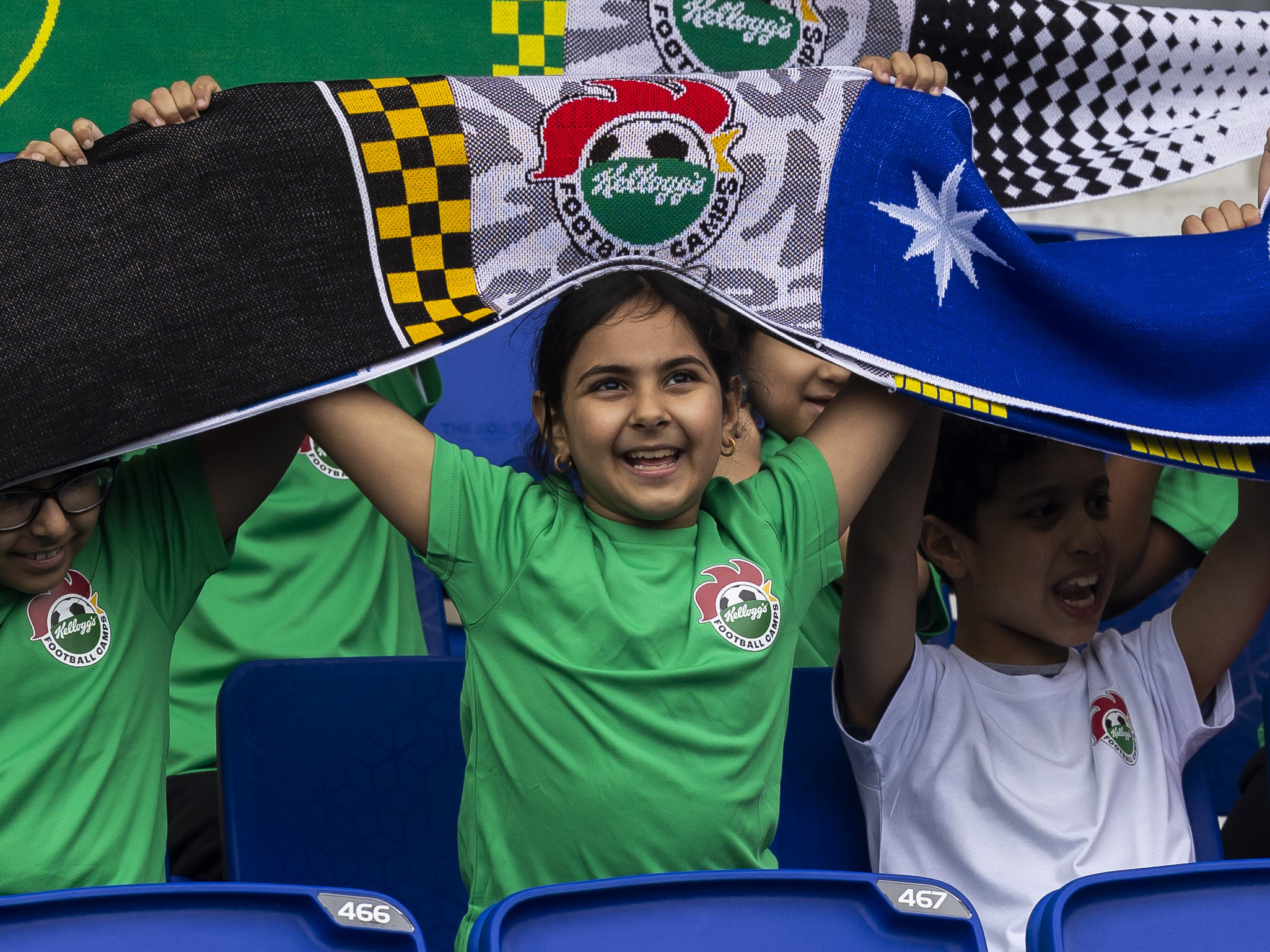 A young girl in a green Kellogg's t-shirt holding up a Kellogg's football scarf 