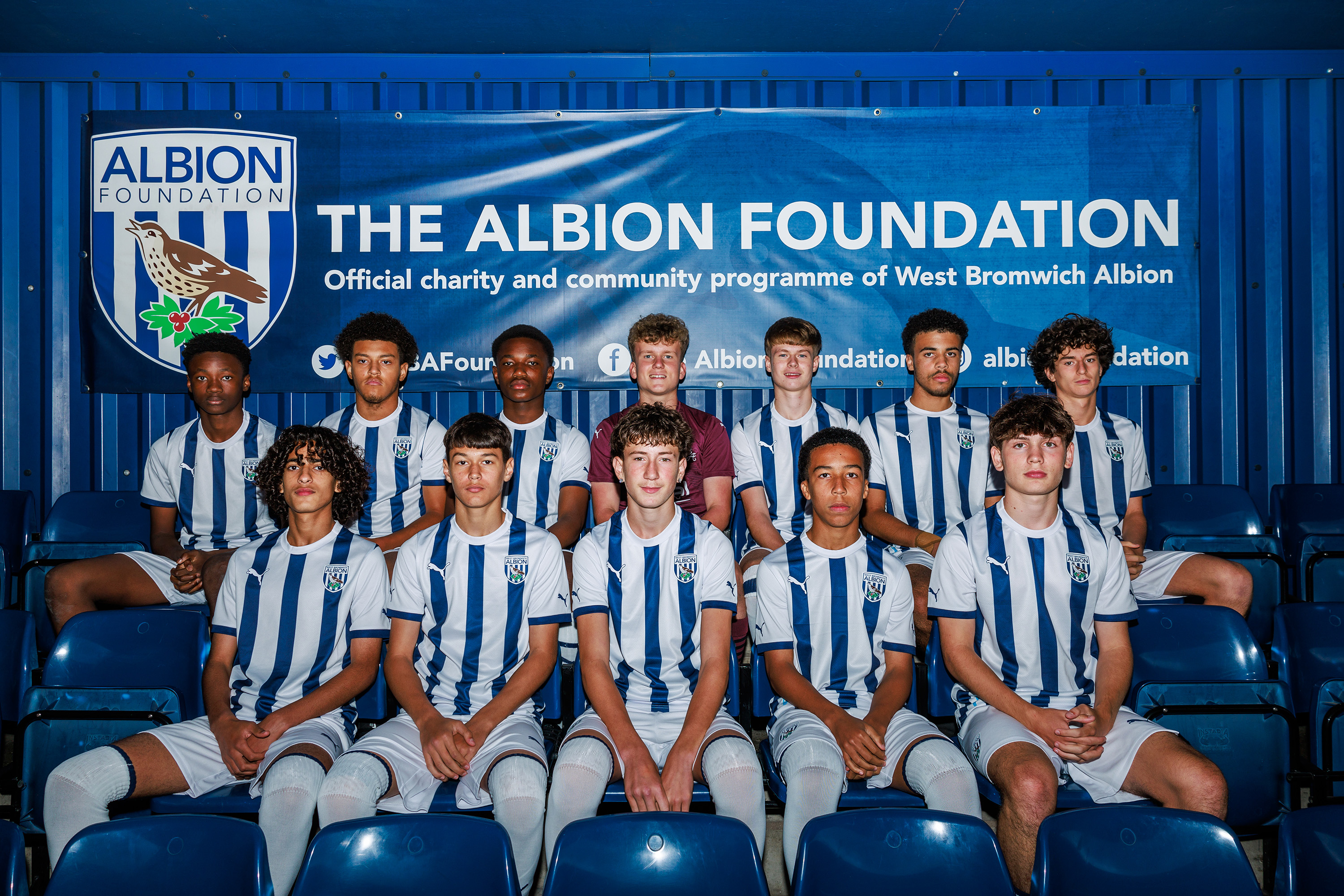 MJPL U16 team seating in the stands under an Albion Foundation banner.
