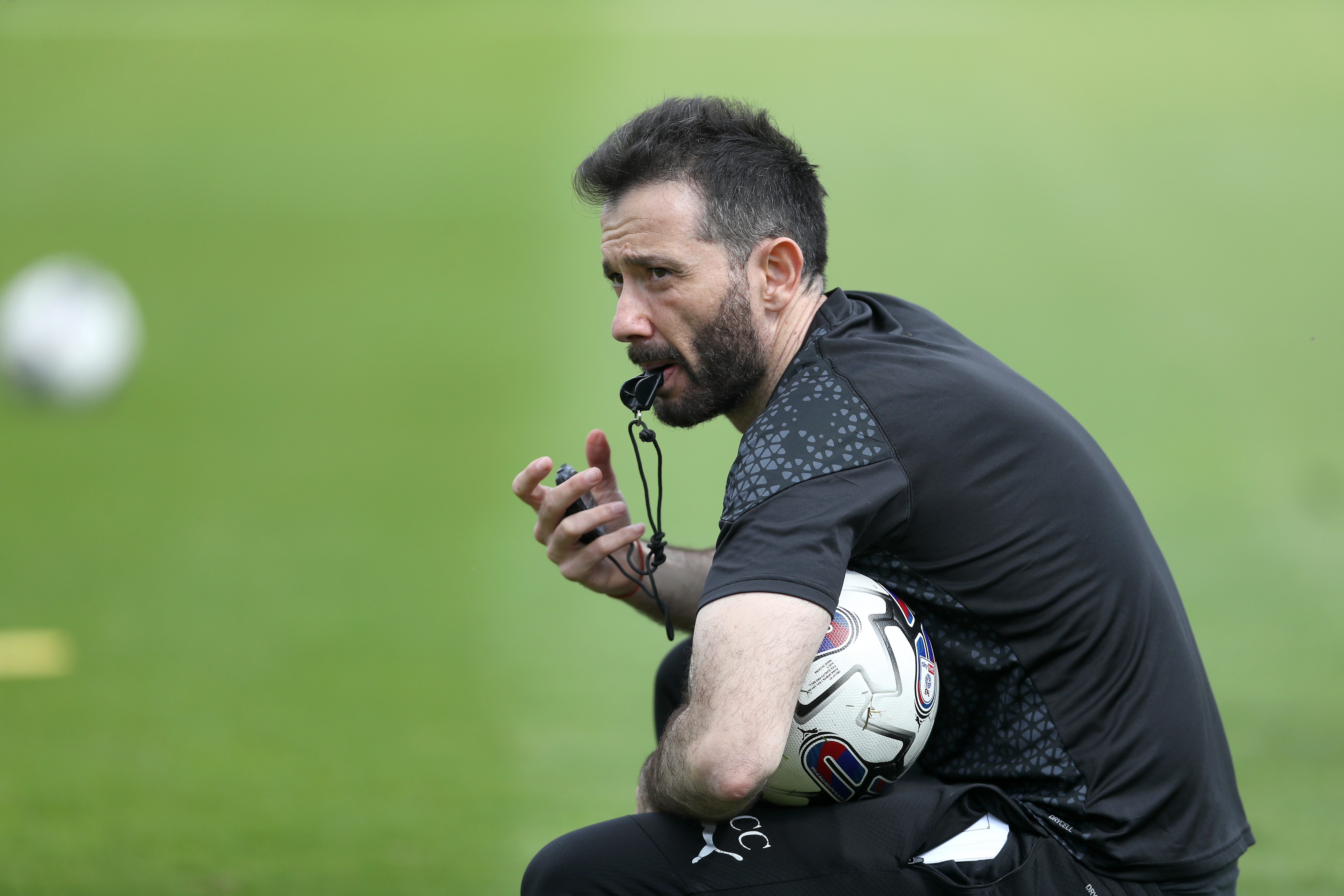 Carlos Corberán crouched down blowing a whistle while holding a ball during training 