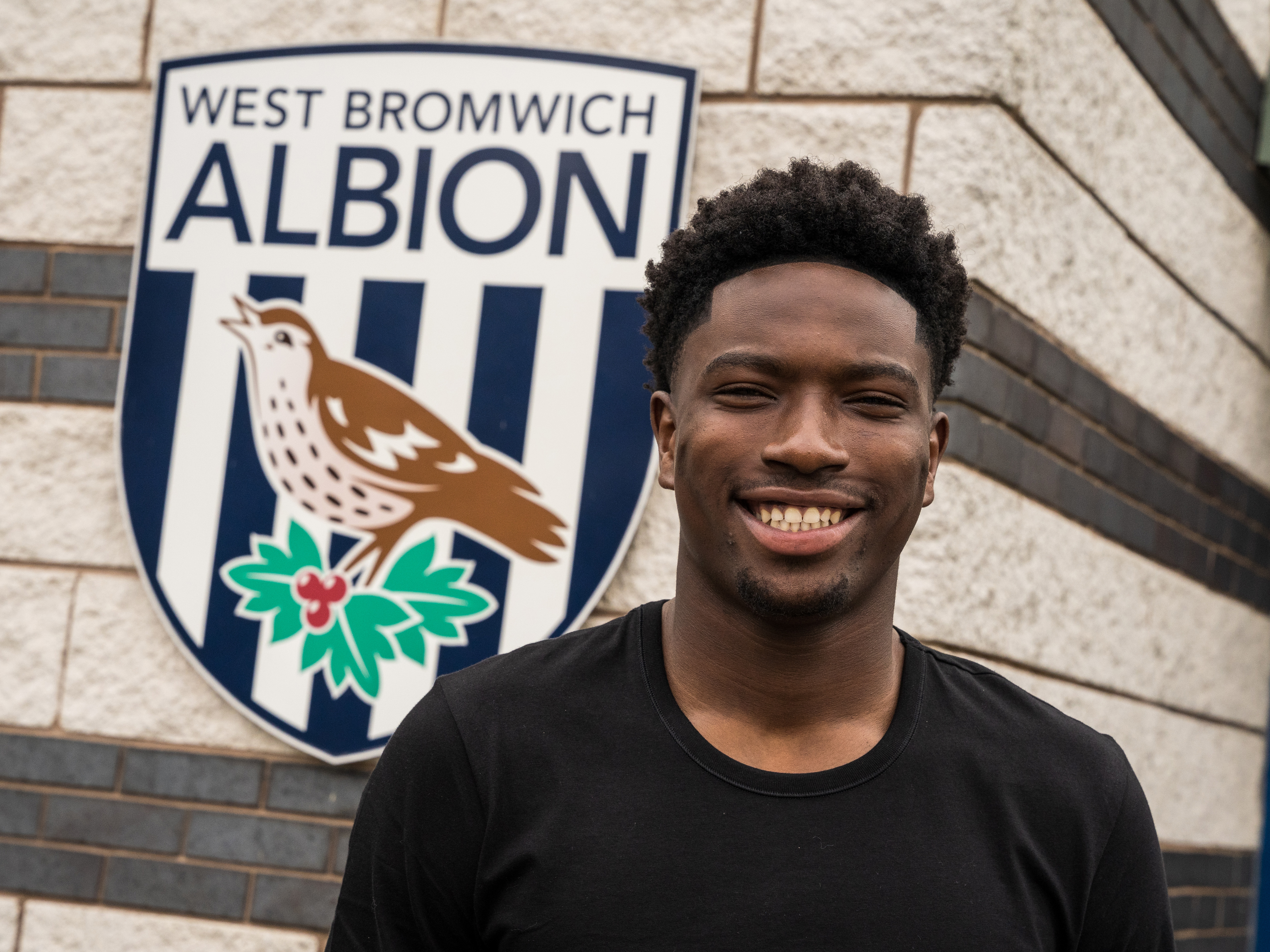 A photo of young goalkeeper Ben Cisse, in front of the Albion badge at the forefront of the Albion training ground