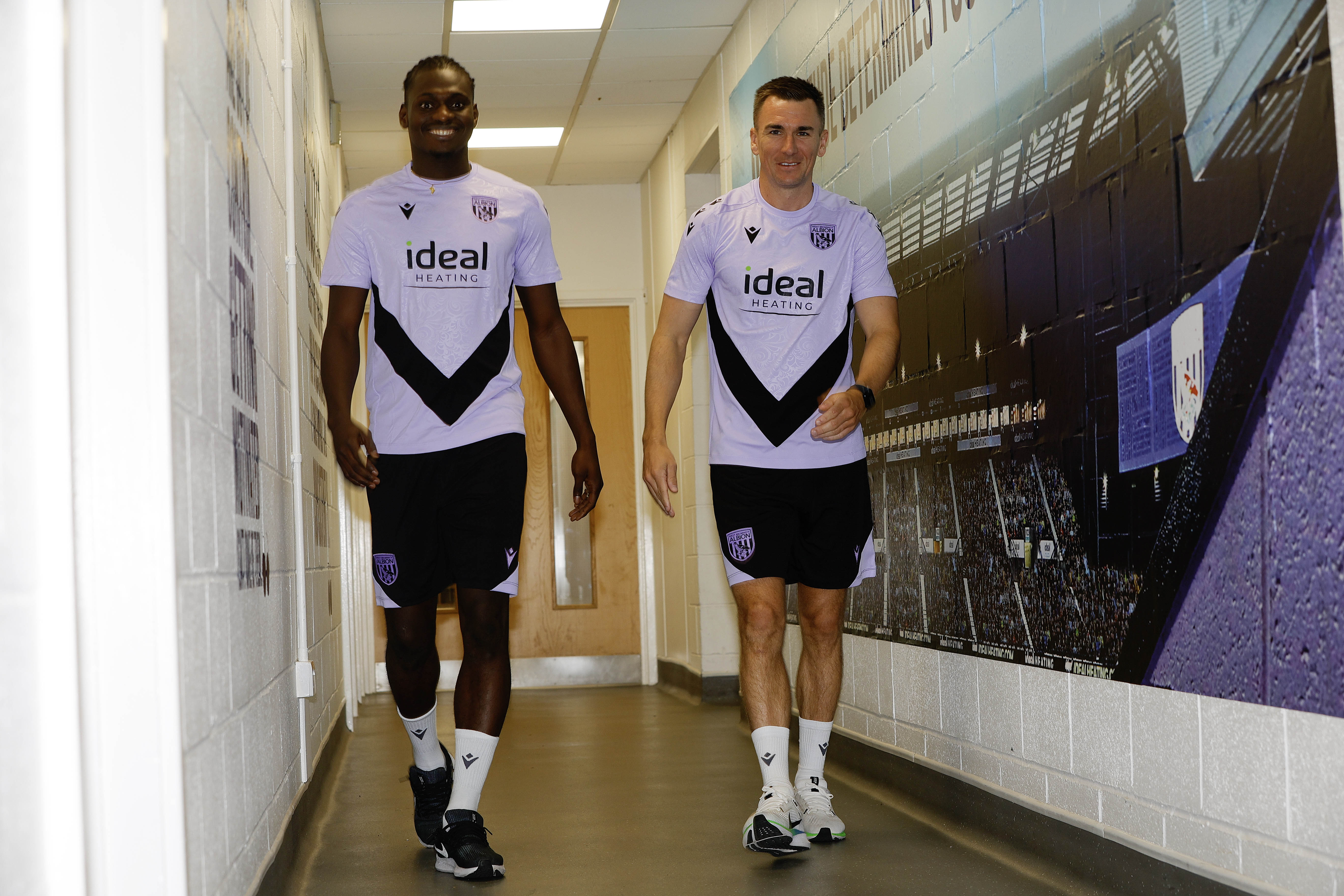 Ousmane Diakité and Jed Wallace chatting while walking down a corridor 