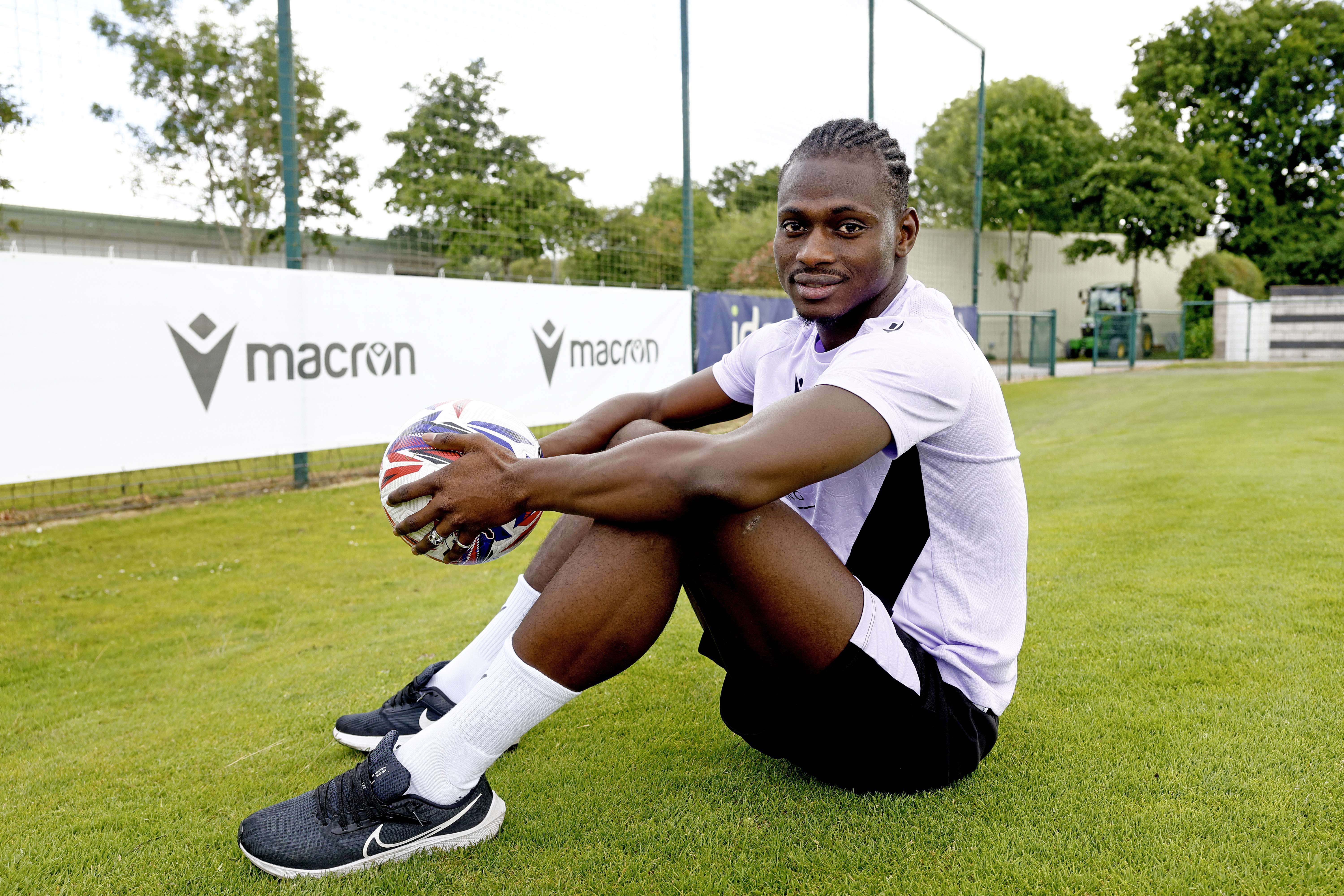 Ousmane Diakité smiling at the camera while sat outside holding a ball