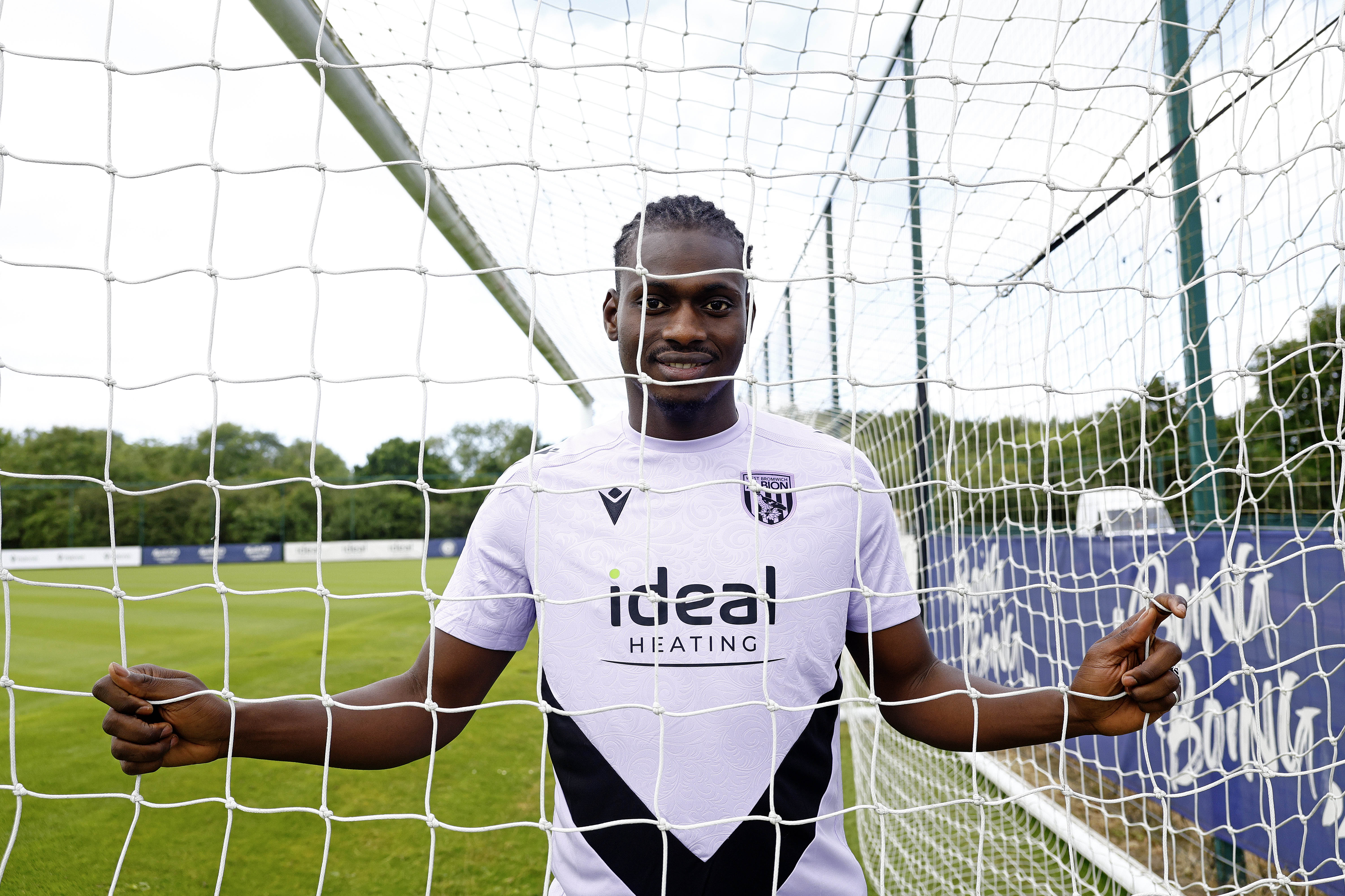 Ousmane Diakité smiling at the camera while holding on to a goal net