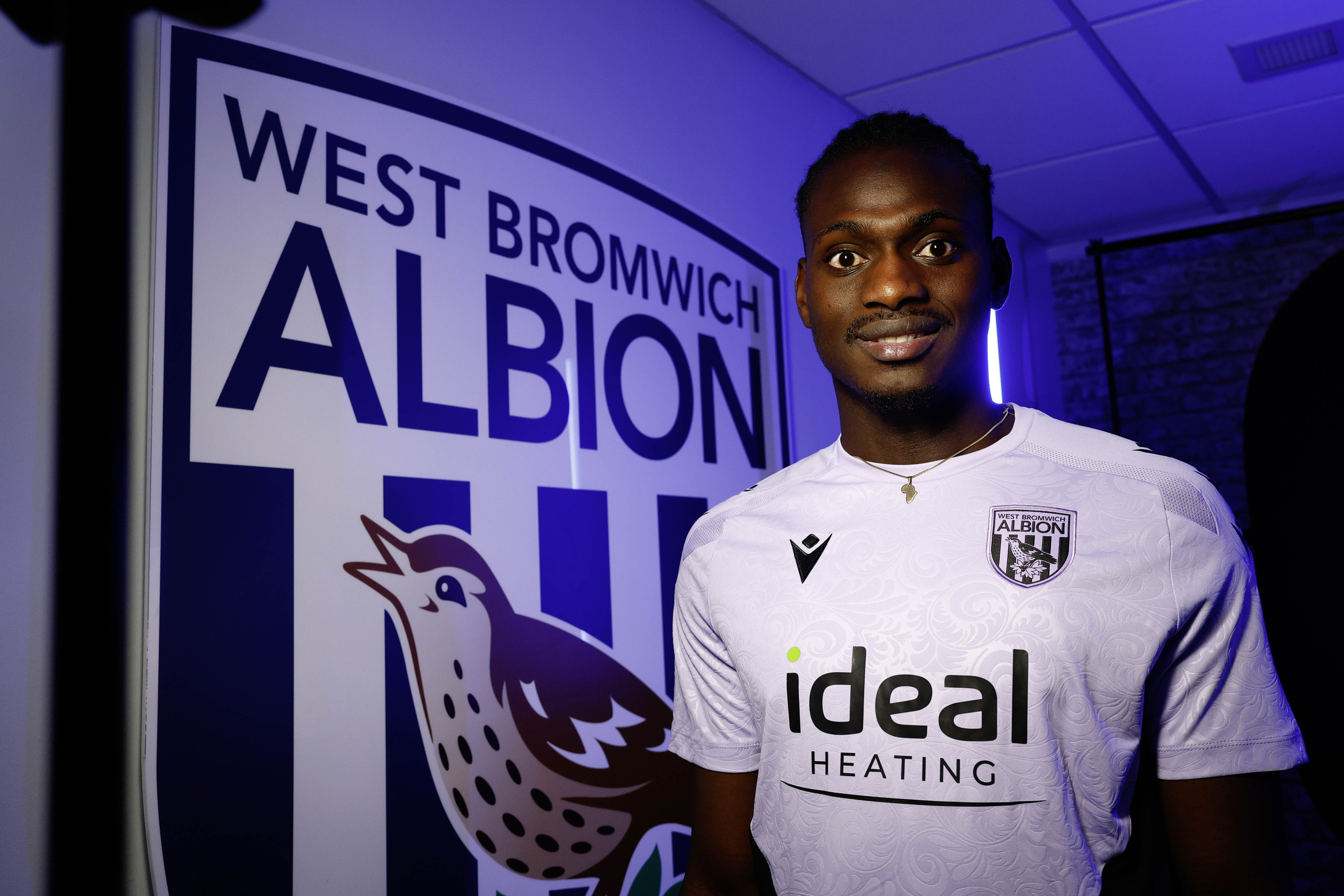 Ousmane Diakité smiling at the camera with a big WBA badge in the background 
