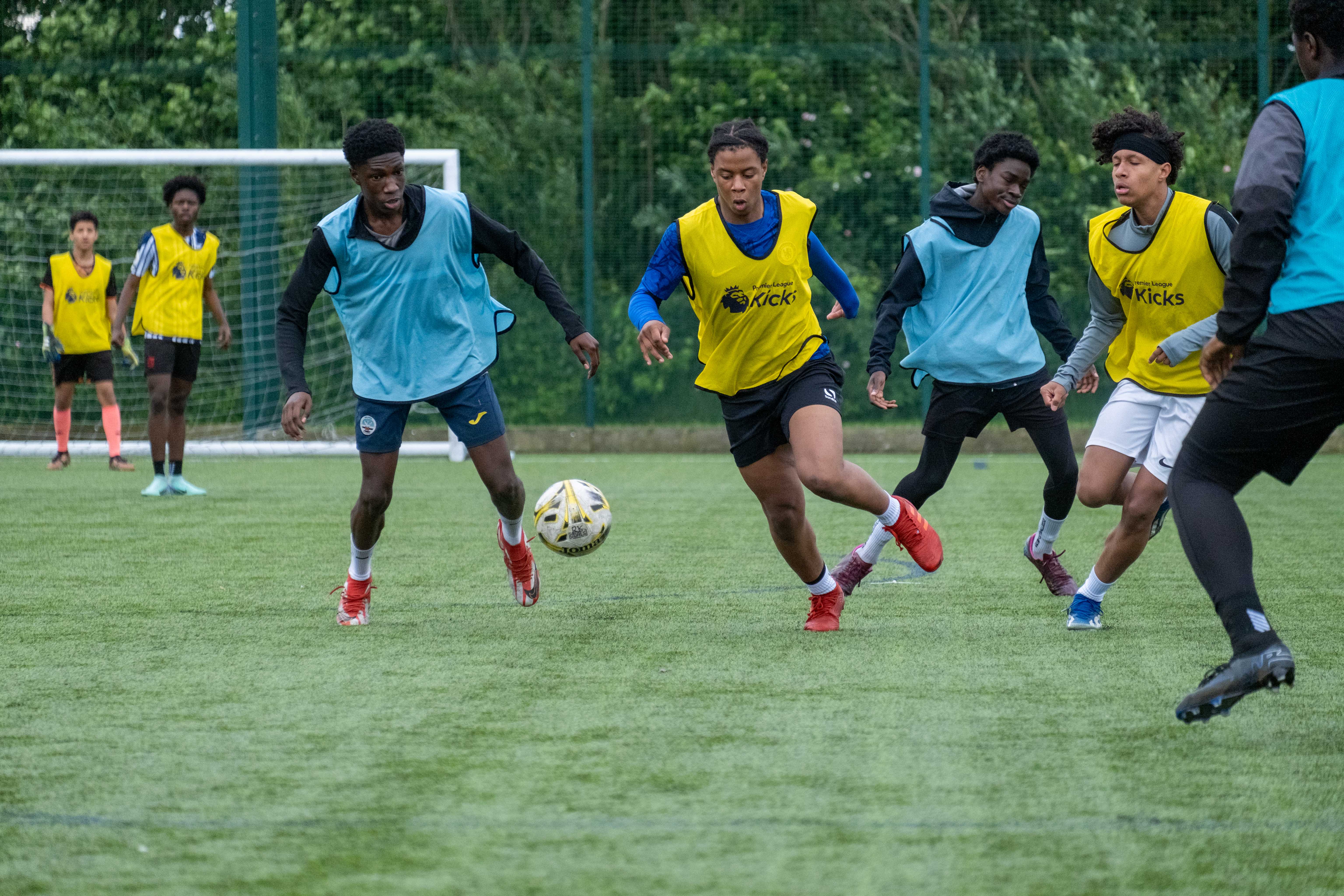 Yellow bibs player chasing the ball, aqua blue players chase.