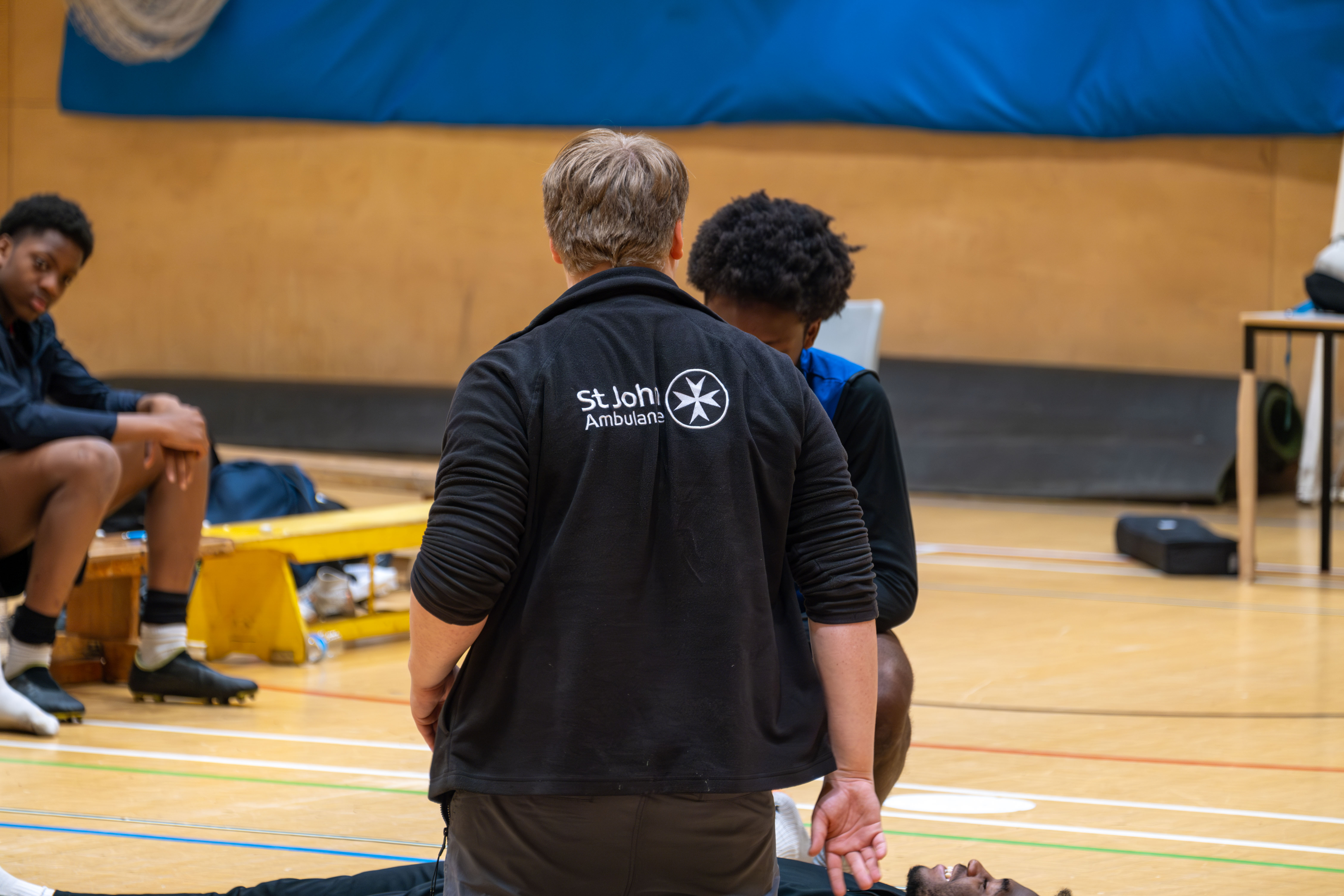 St John's Ambulance tutor (back to camera) demonstrating how to check for danger.