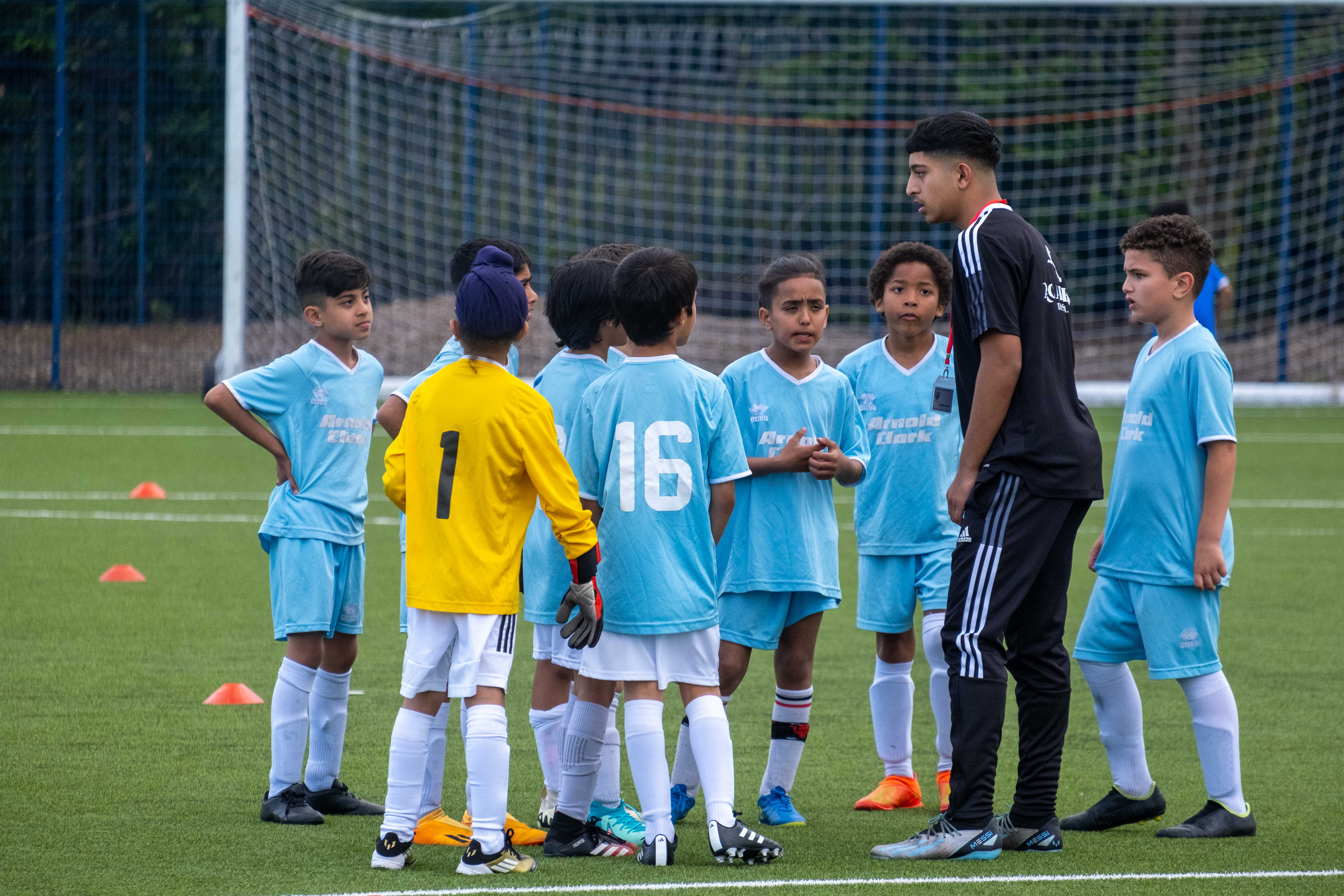 A coach gives instructions to a team wearing sky blue at the South Asian Emerging Talent Festival on the Academy pitch.