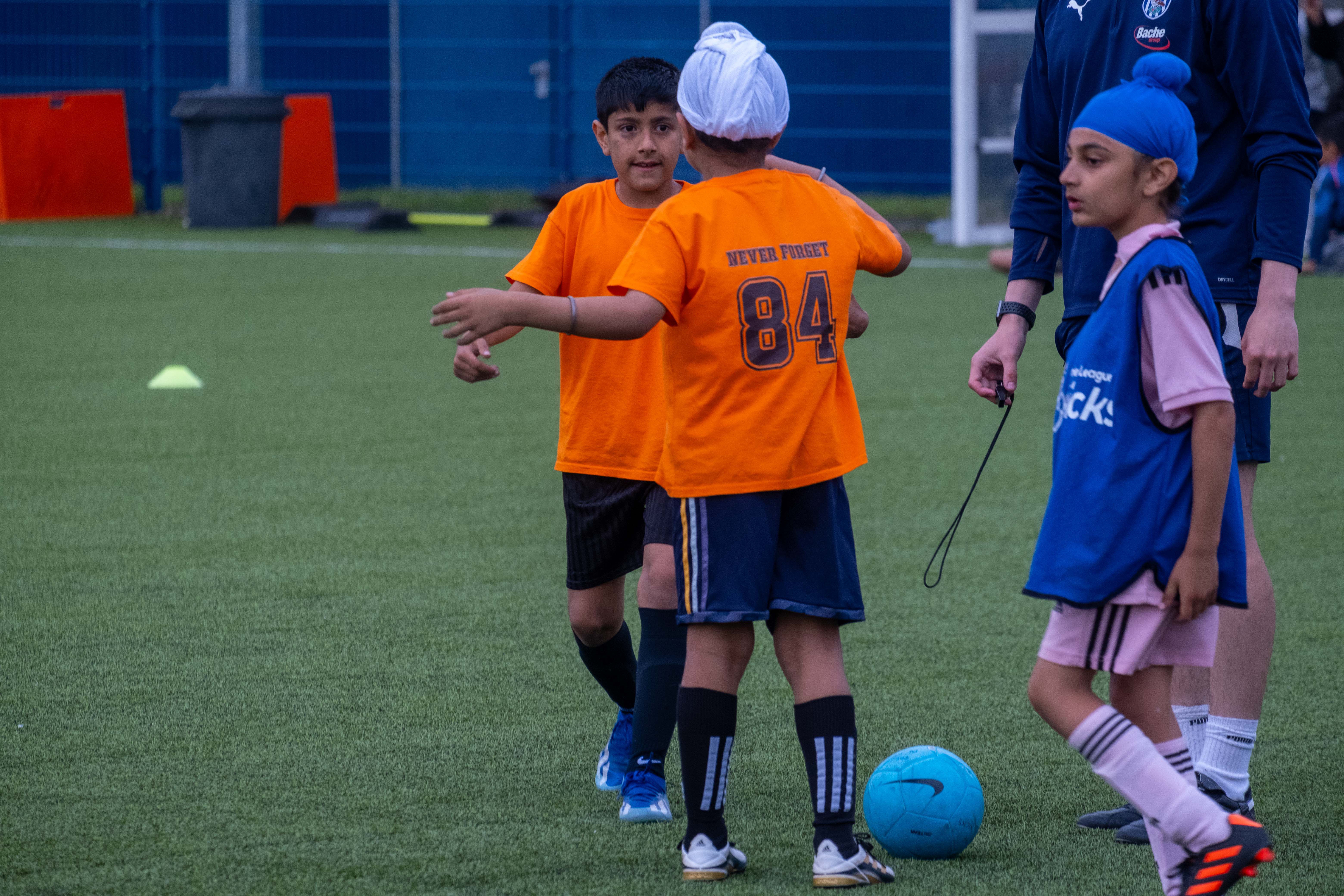 Players wearing orange shirts go to hug each other during the South Asian Emerging Talent Festival on the Academy pitch.