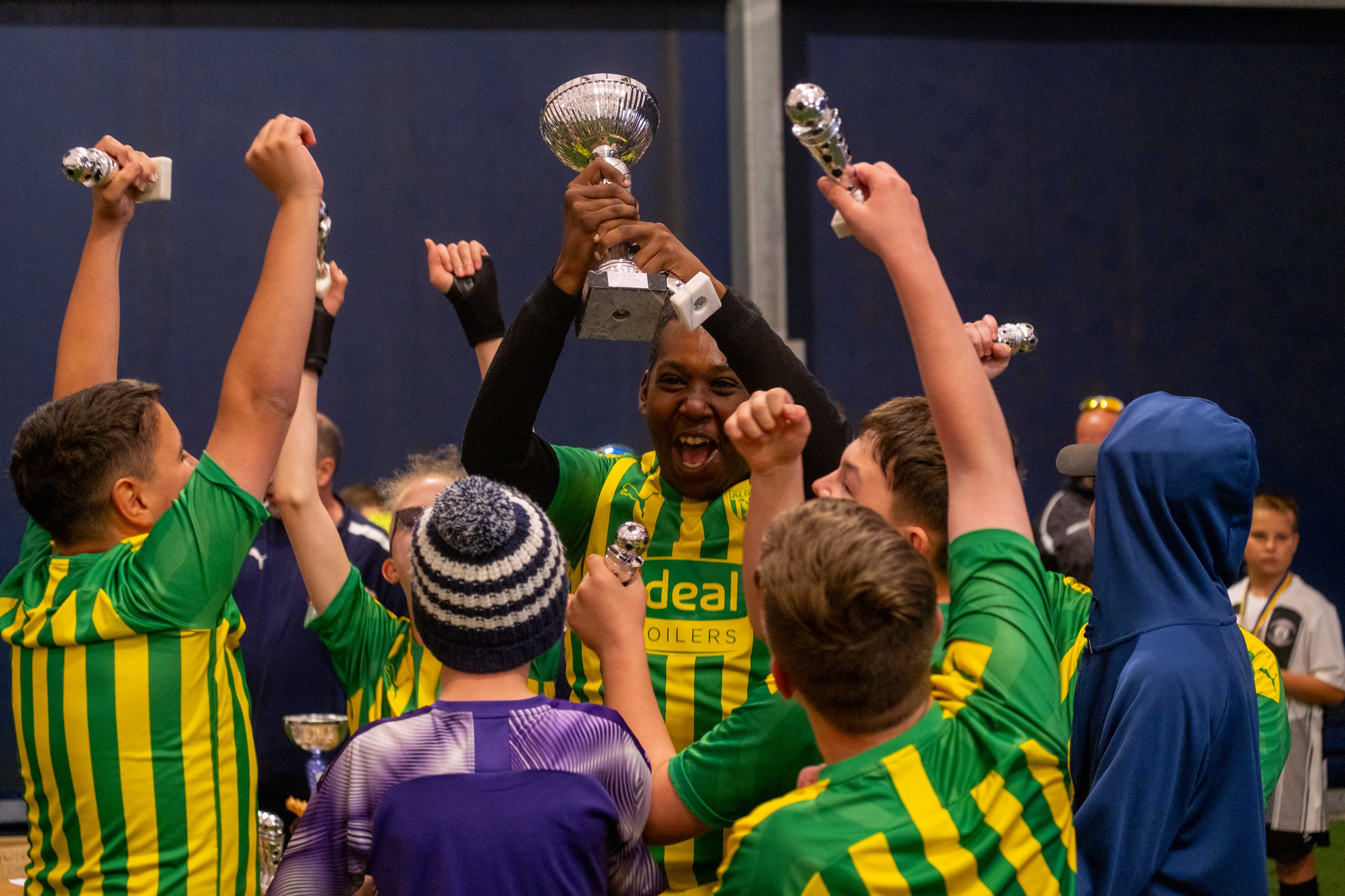 A group of Albion players lift one of the Sandwell Inclusion Cup trophies wearing the Baggies' 2019/20 green and yellow away shirt.