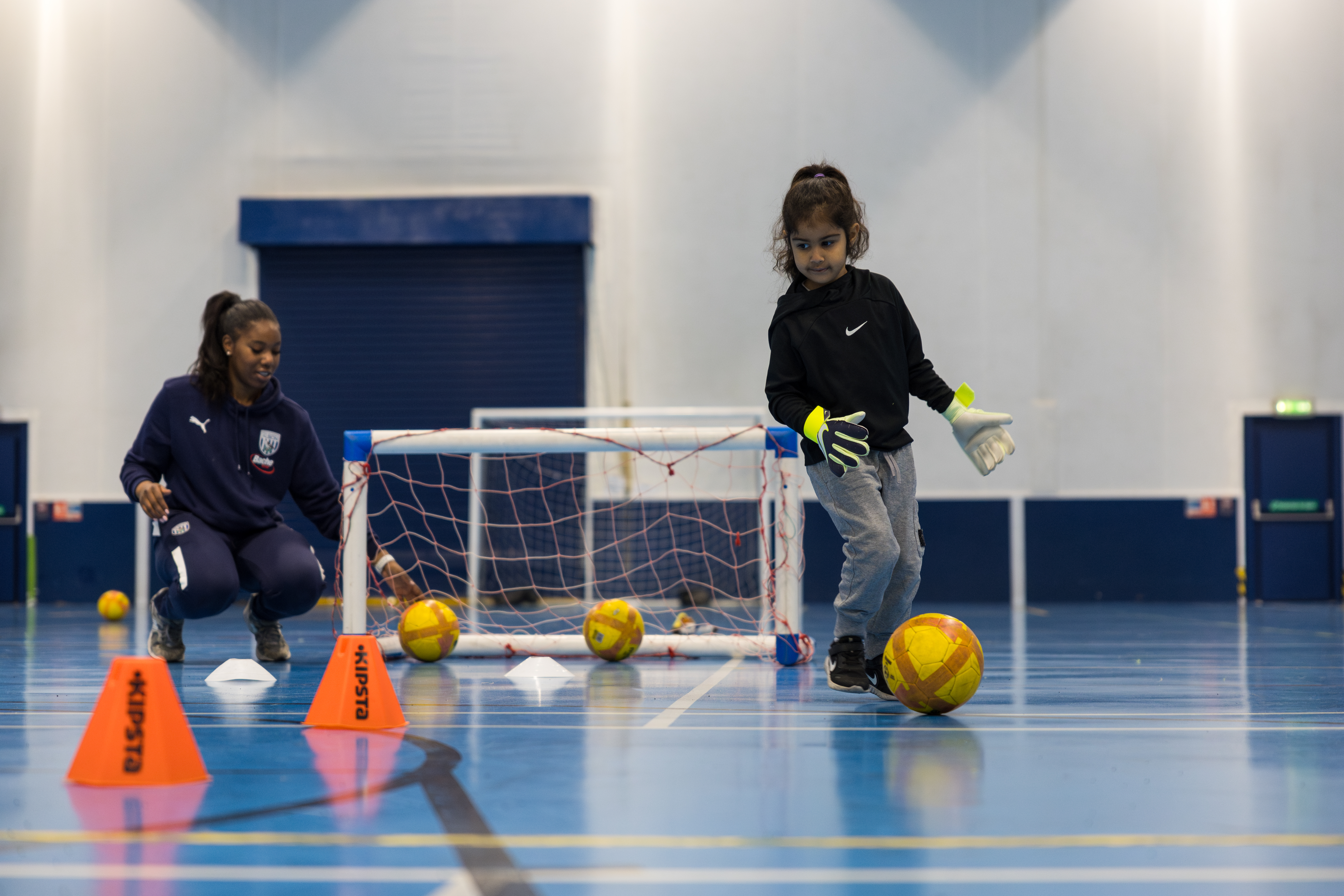 Khadijah dribbles the ball forwards whilst being watched by an Albion Foundation coach.