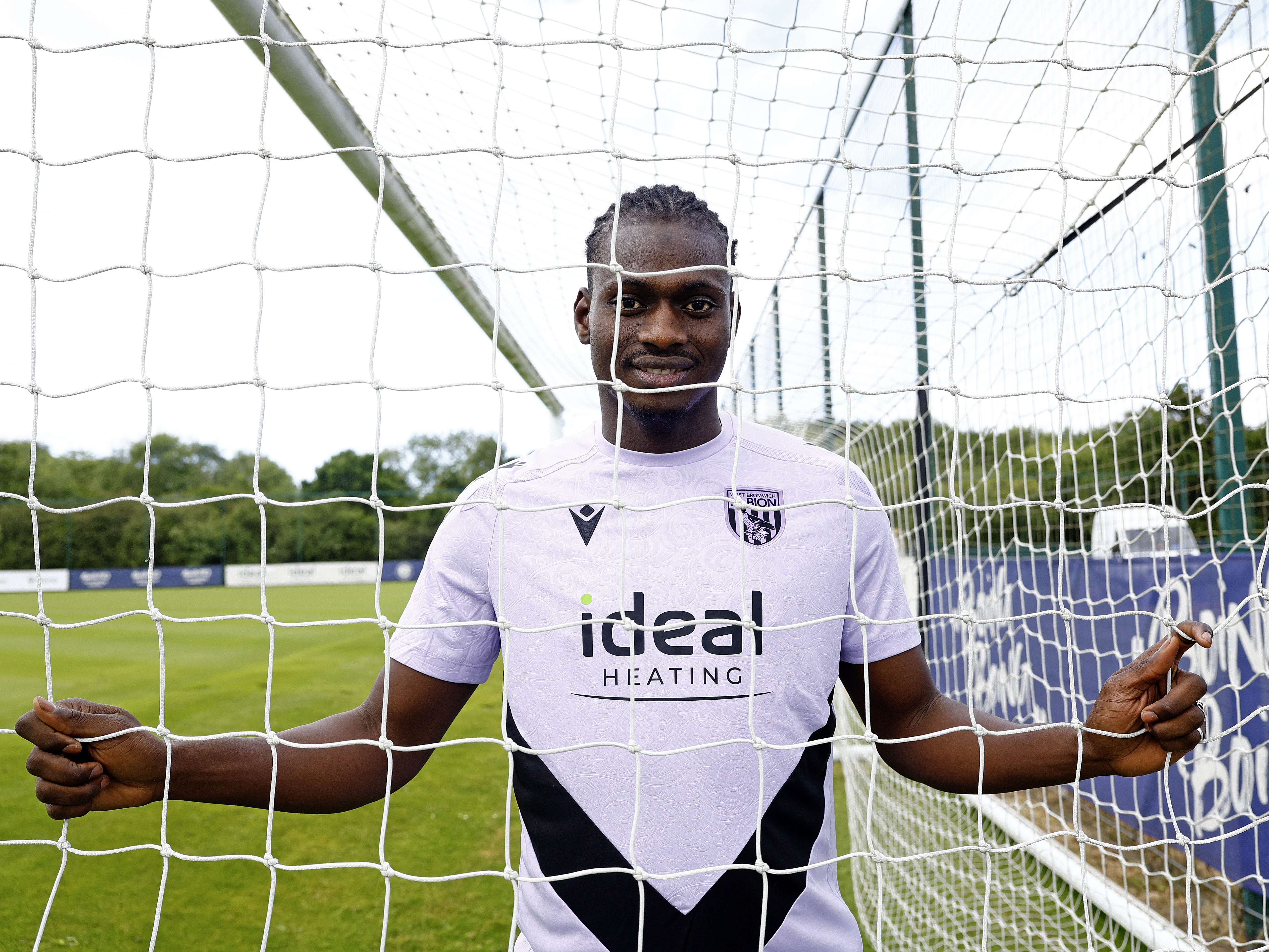 Ousmane Diakité smiling at the camera while looking through a goal net