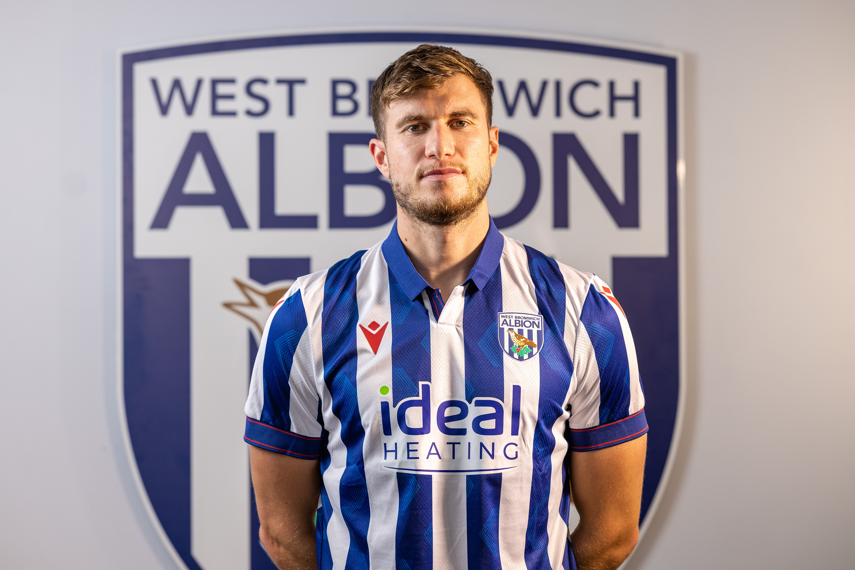 Paddy McNair looking at the camera while wearing a home shirt stood in front of an Albion badge 