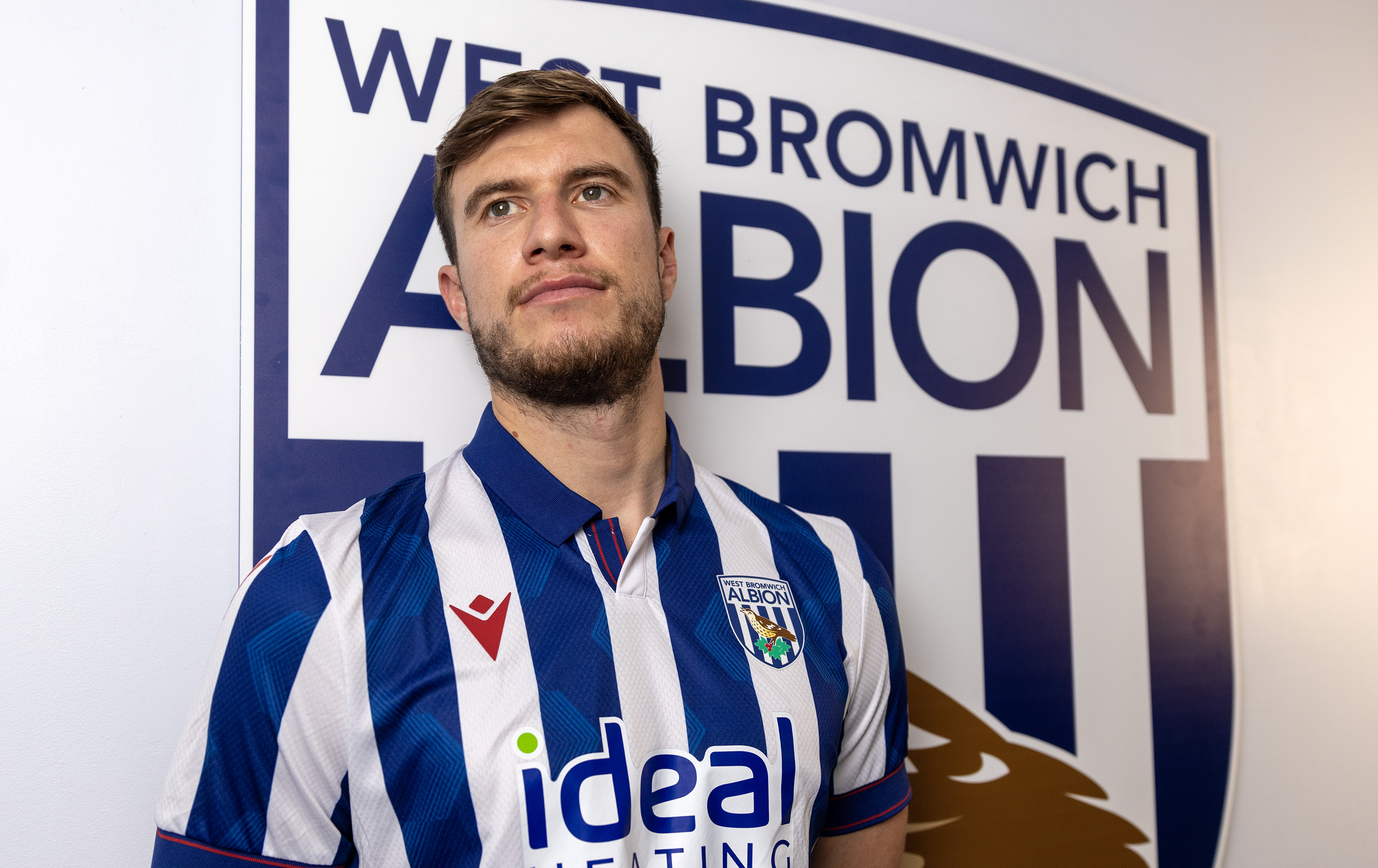 Paddy McNair looking away from the camera while wearing a home shirt stood in front of an Albion badge
