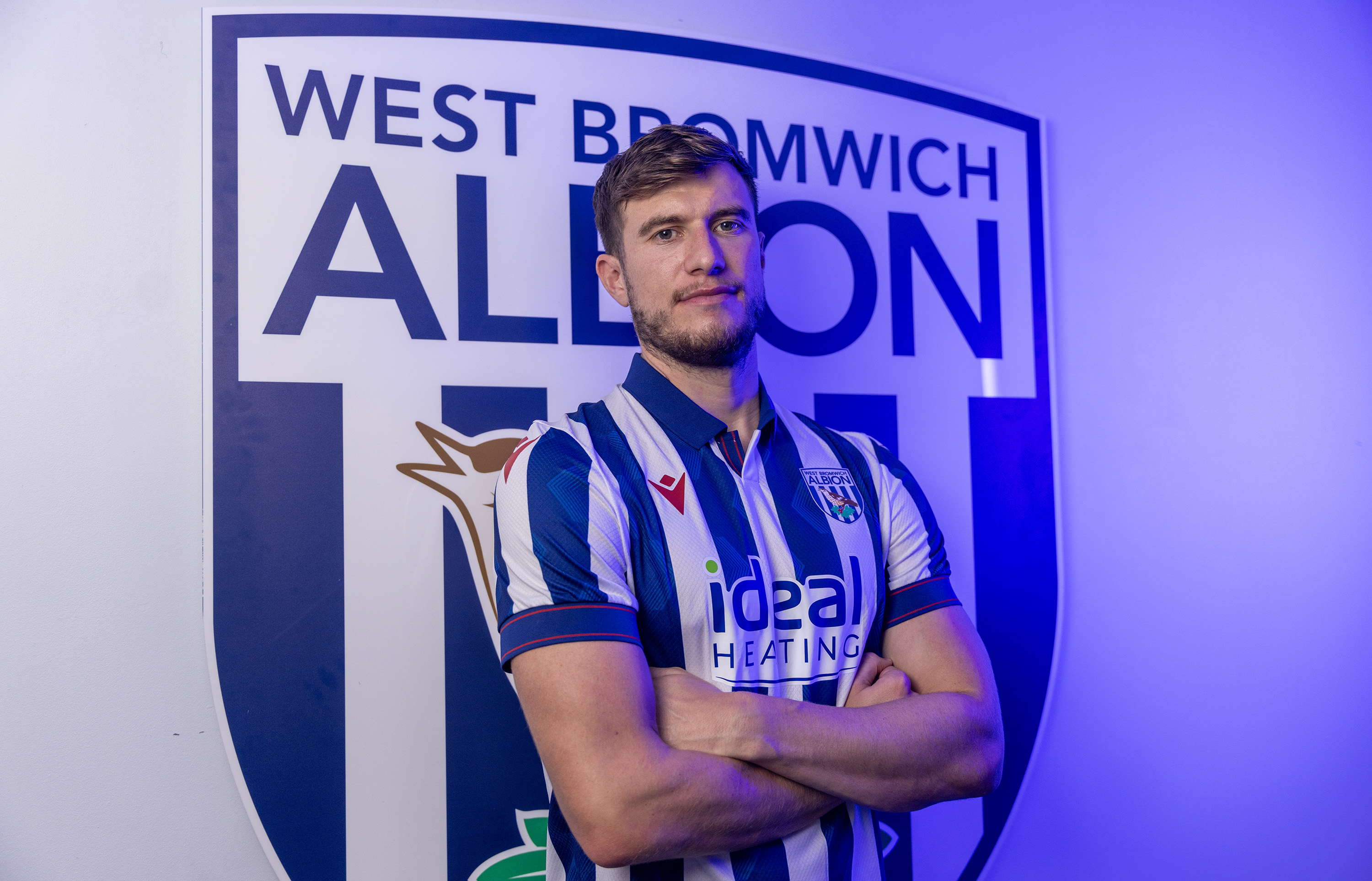Paddy McNair smiling at the camera while wearing a home shirt stood in front of an Albion badge