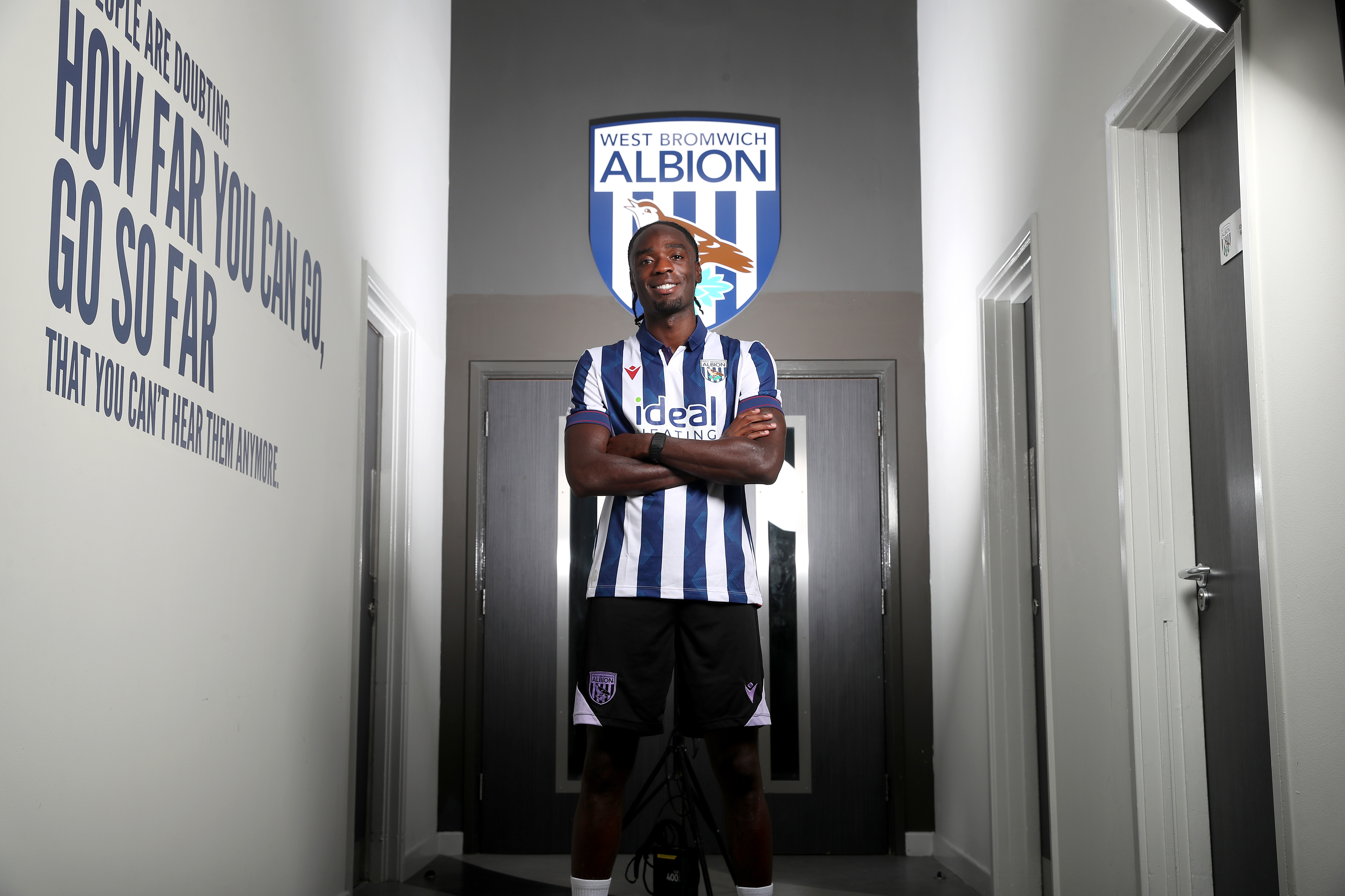 Devante Cole with his arms crossed smiling at the camera wearing a home shirt 