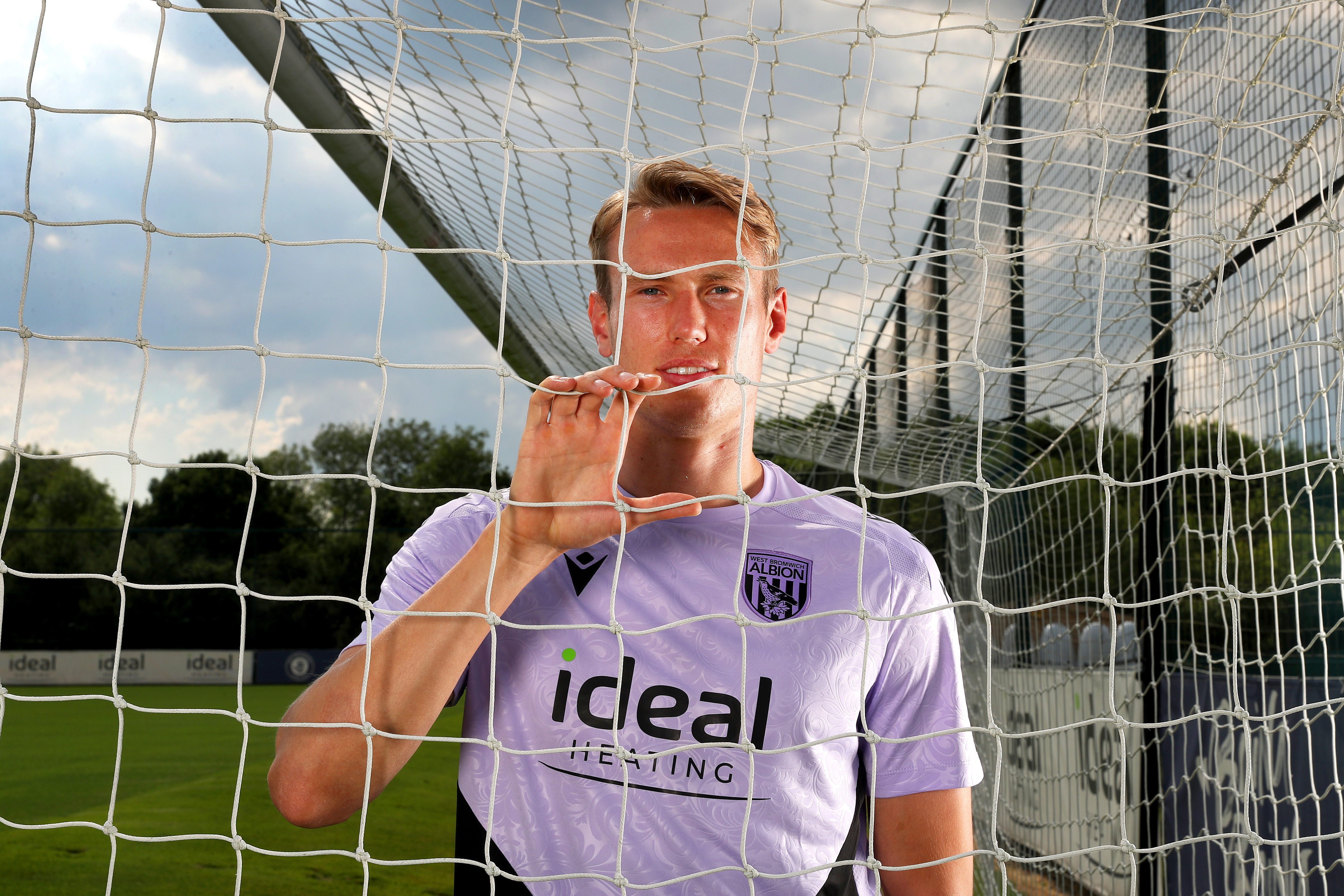 Torbjørn Heggem smiling at the camera while looking through a goal net