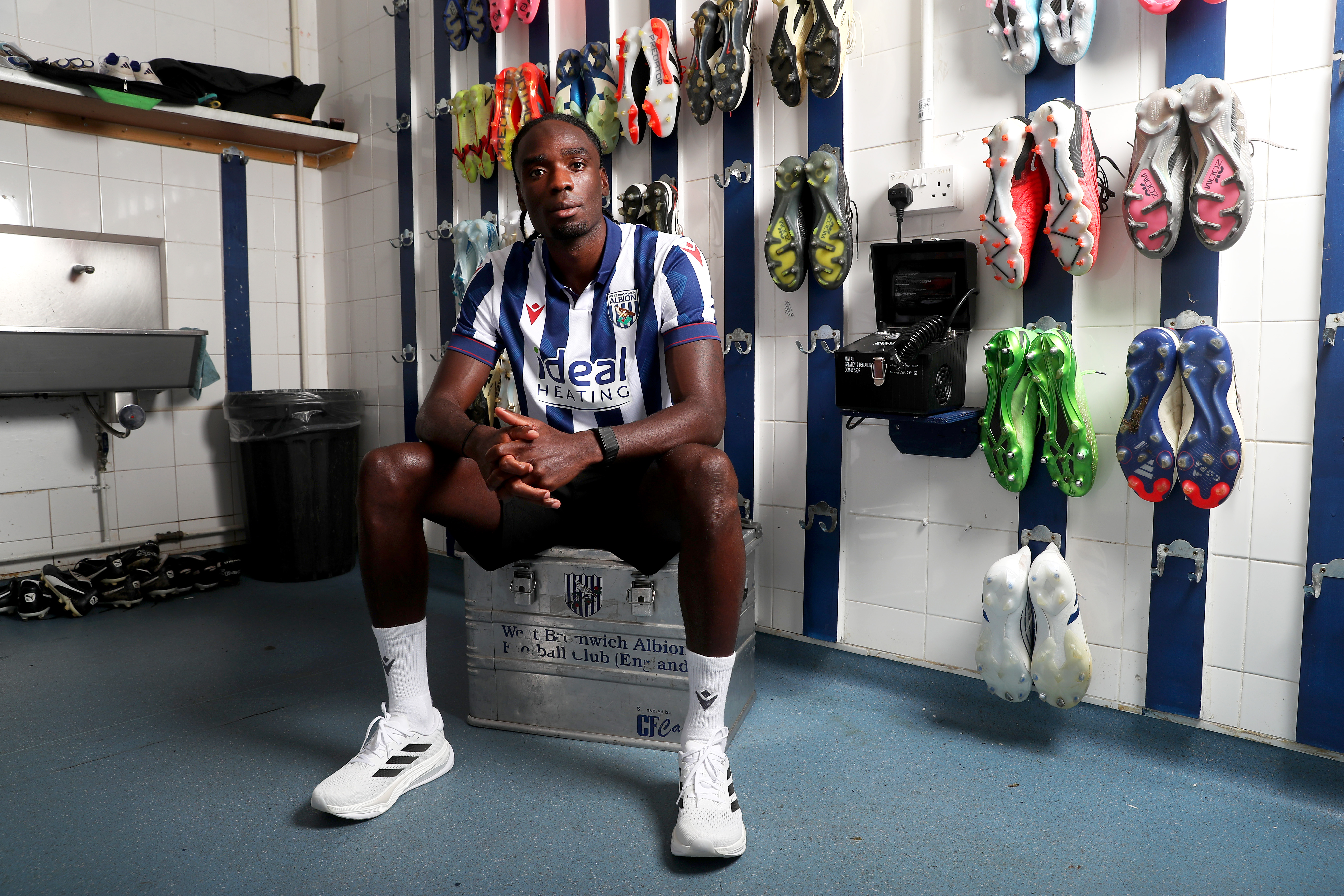 Devante Cole staring at the camera in a home shirt while sat in the boot room