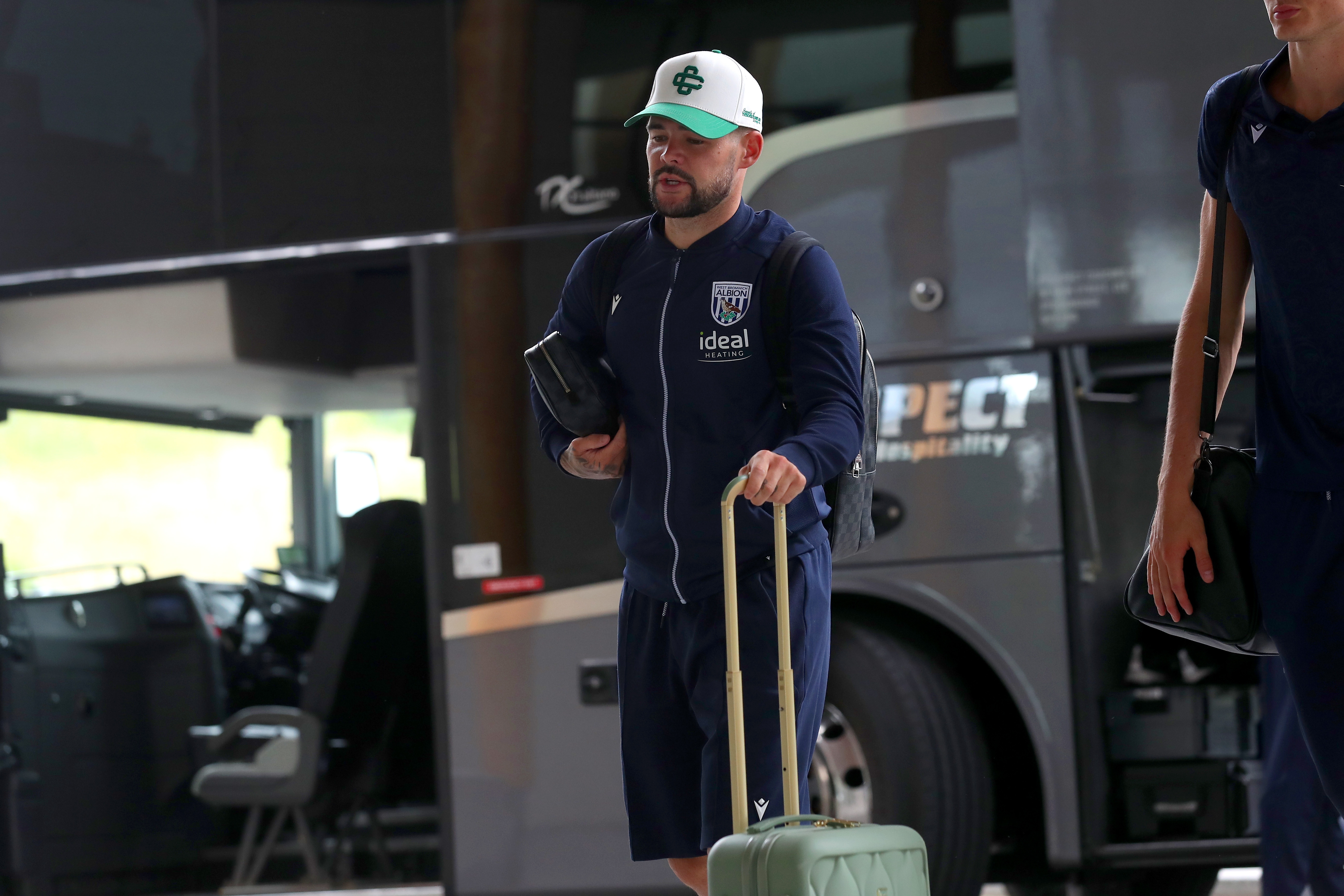 Alex Mowatt arriving at St. George's Park pushing a suitcase wearing a cap